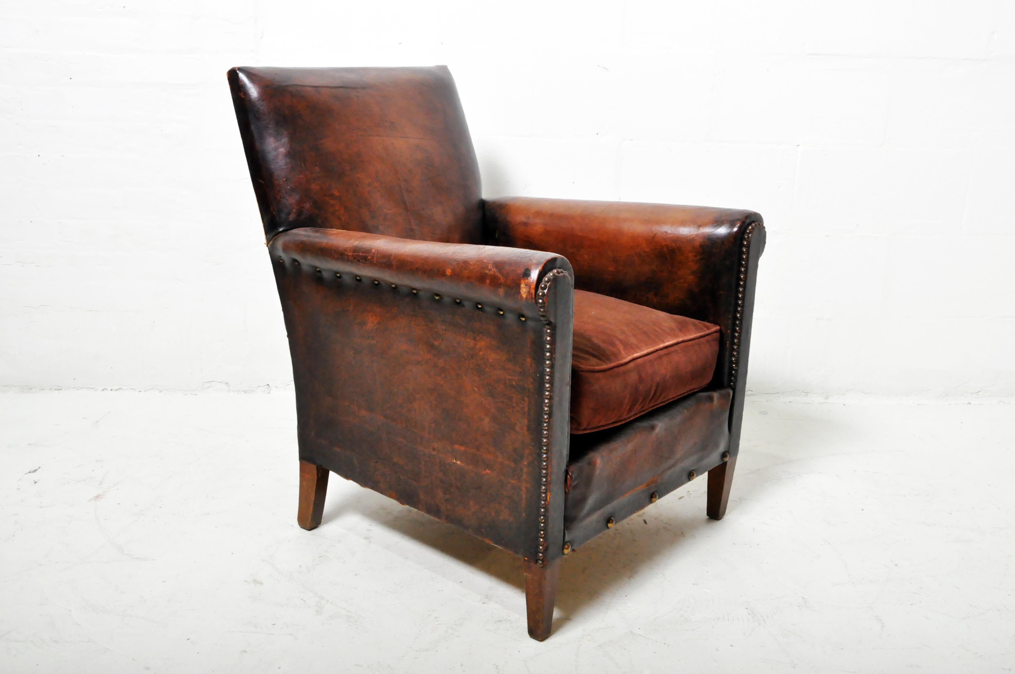 This petite 1930's leather club chair has a richly aged patina and tasteful proportions.  The soft lamb leather is  without large tears or gashes --good condition, considering its age and use.   The nailheads are almost all original, with only a few