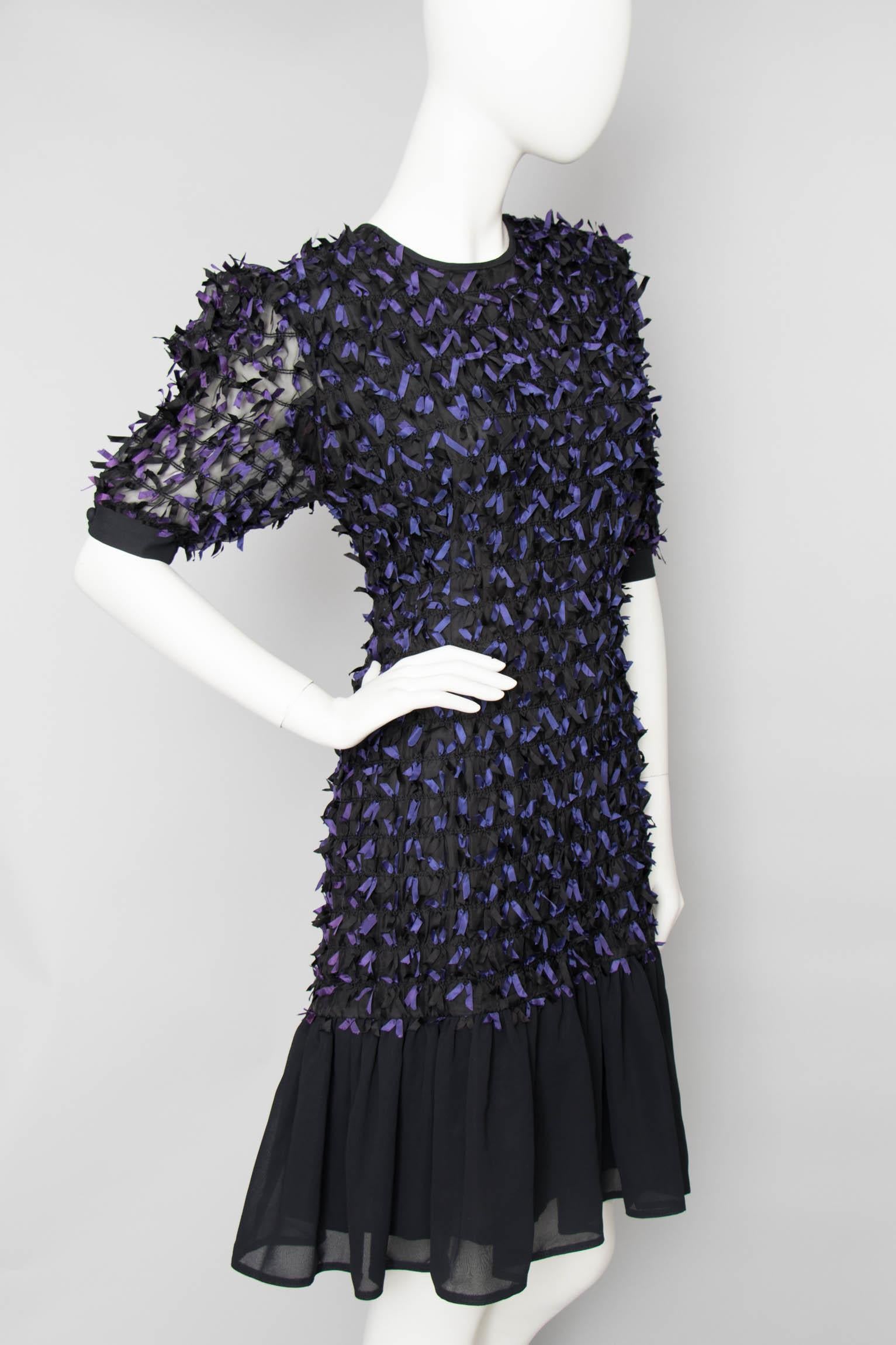 A 1980s Givenchy En Plus black cocktail dress with a round neckline, puffed shoulders and a ruffle hemline. Small purple and black bows cascade down the dress and short sheer sleeves. The dress is fully lined. 

The size of the dress corresponds to