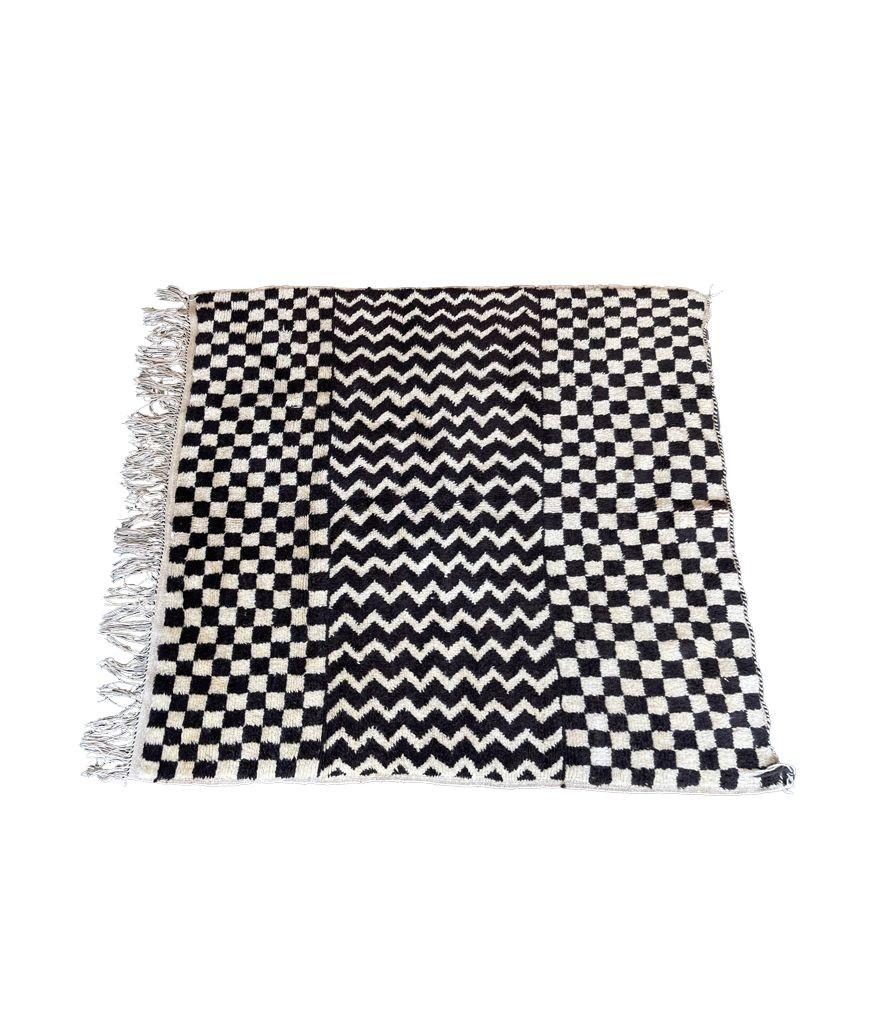 A vintage 1970s handmade Moroccan chequerboard and zig zag pattern, Berber rug in black and white handwoven wool by the Beni Quarian tribe. A wonderful geometric design with wool tassels down one side and black and white twisted thread on the other.