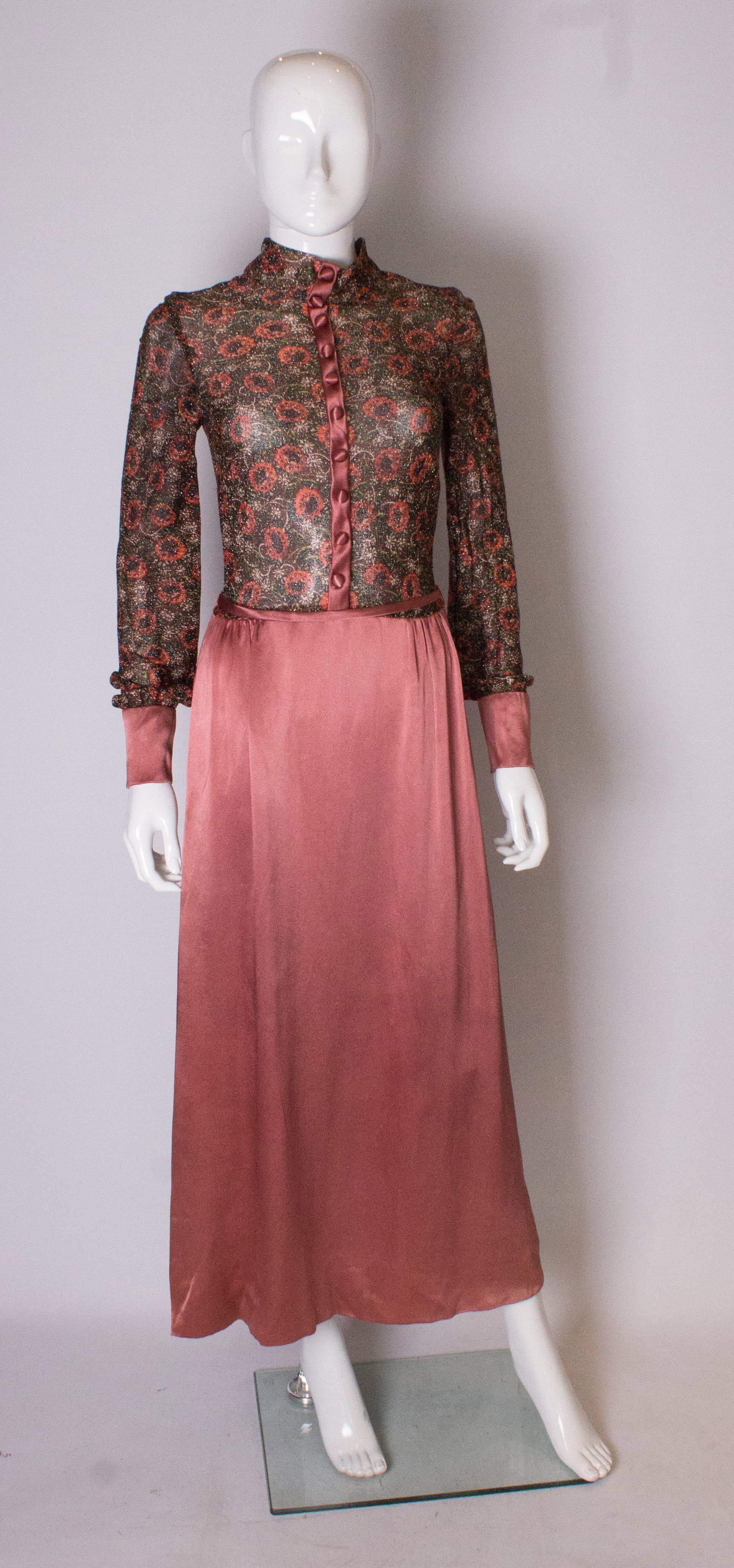 A stunning 1970s gown by Jean Varon. The upper part is a soft gold colour lurex with a floral design. The lower skirt area is a dusty pink colour. The dress has wide cuffs with four buttons and there are ten decorative covered buttons on the front.
