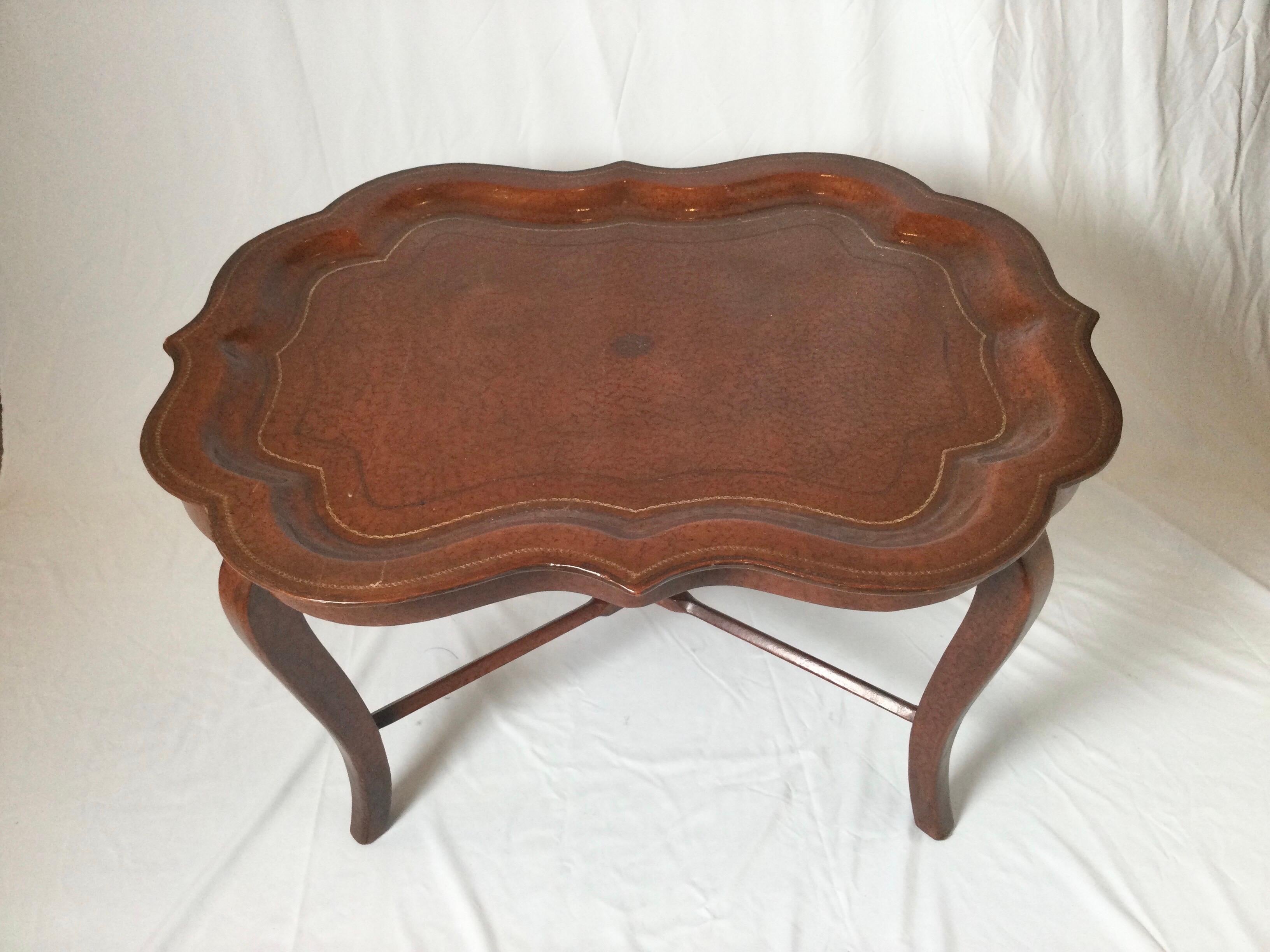 Unigue tray top table with leather surface. The scalloped tray with original base, leather covered hardwood with gilt decoration. Beautifully shaped with tray top that lifts.