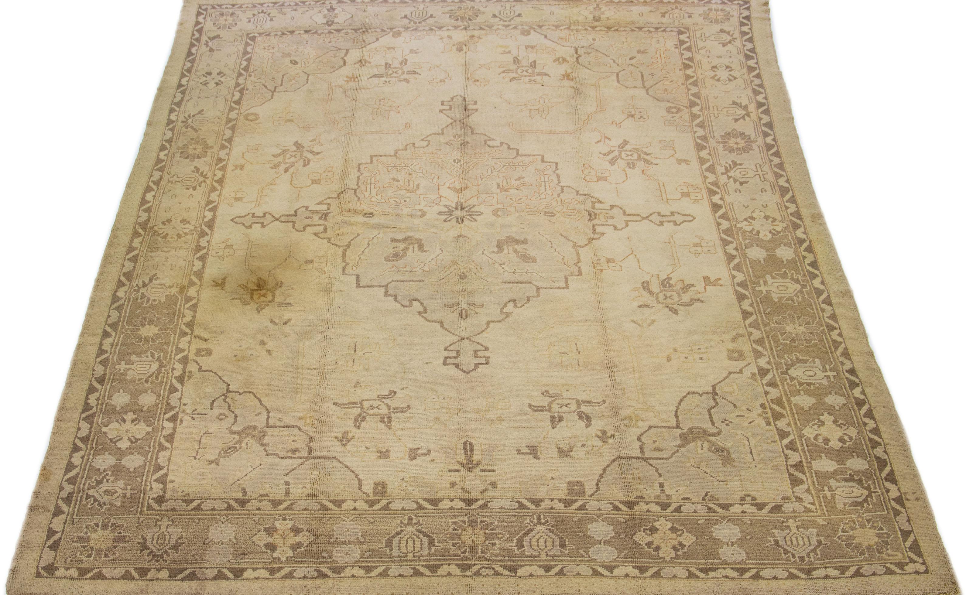 Cet exceptionnel tapis en laine turque de style antique présente une charmante base de couleur beige et est noué à la main avec la plus grande attention aux détails. Avec de superbes accents bruns, il présente un motif floral médaillon