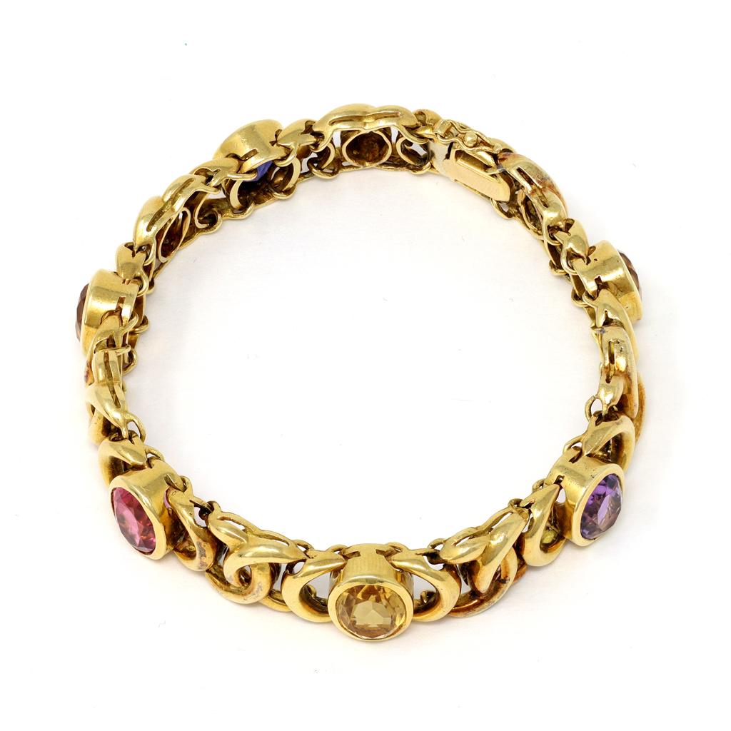A vintage and colorful bracelet made in Italy, featuring multicolor calibrated oval shape gemstones like citrine, iolite, amethyst and pink tourmaline circa 1980. The stones are bezel set and spaced with intricate rounded gold links. Each stone has