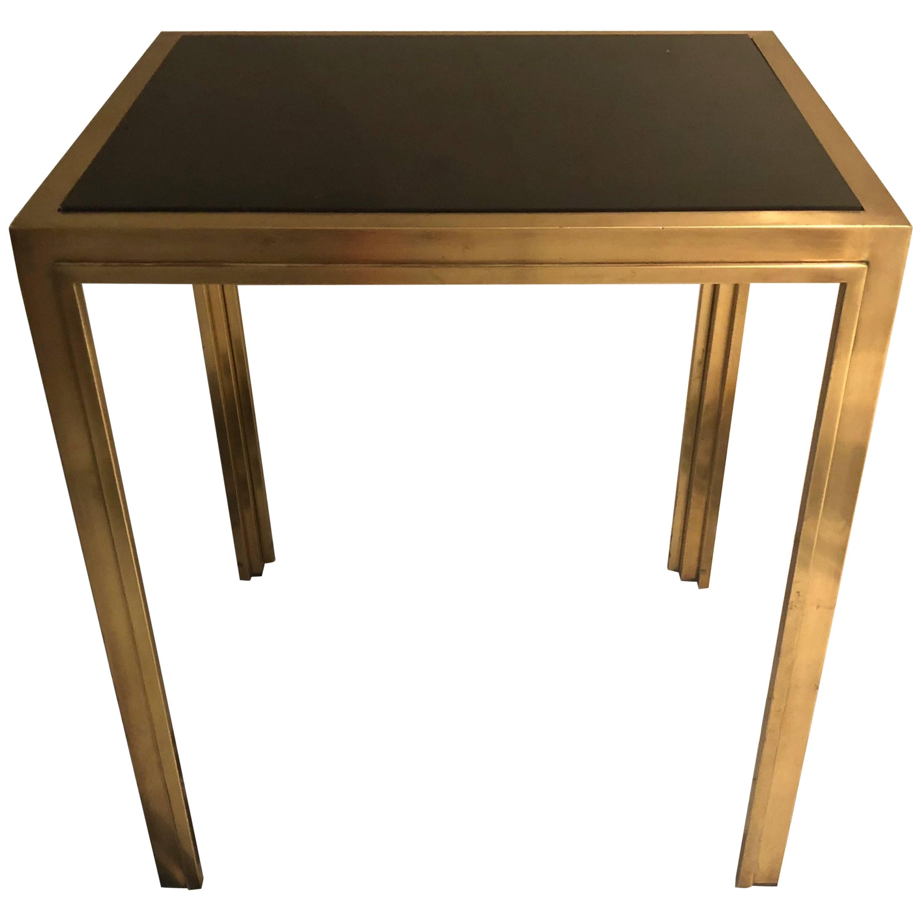 A pair of French deco side tables with an inset black glass top. Each table has the original brass over bronze finish with a decorative trim along the inside edges.
Tables were purchased in France and said to come from the lobby of a building in