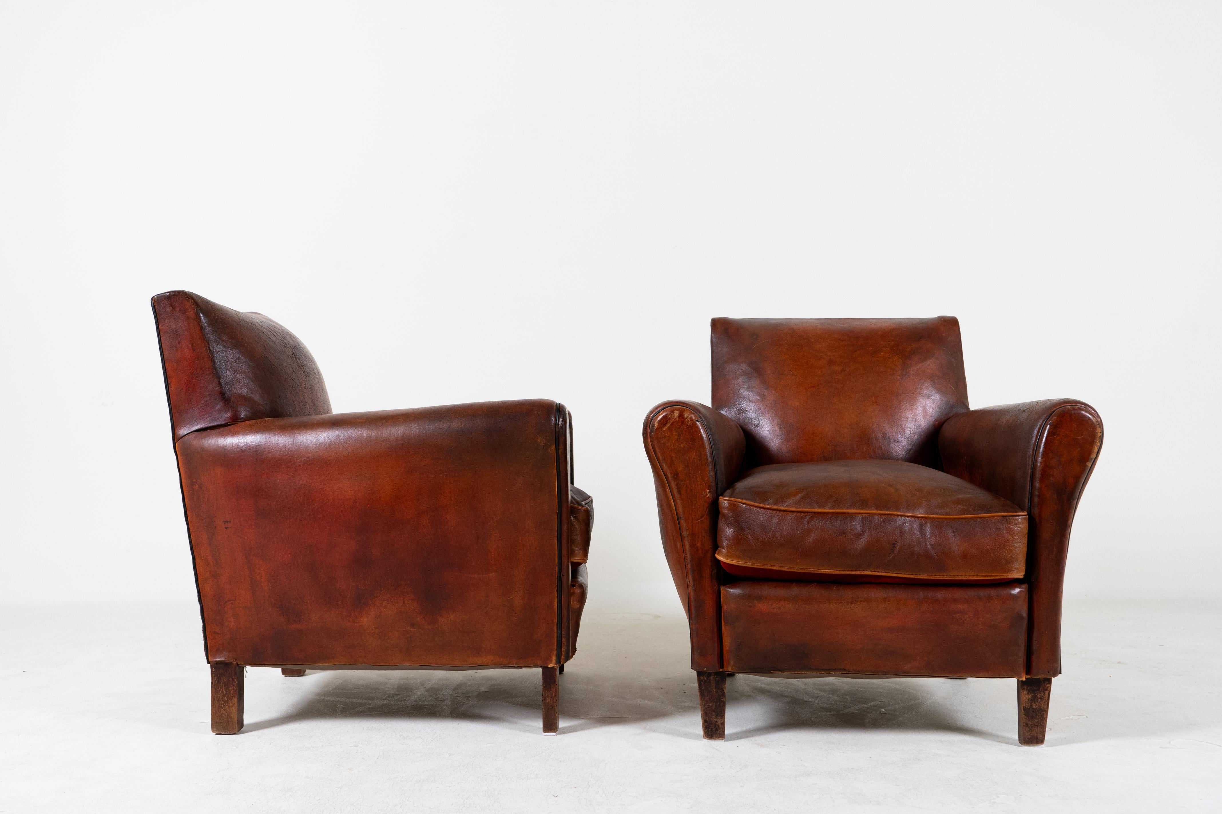 This pair of vintage French Art Deco club chairs dates to the height of pre-war modern design. While many furniture pieces of the Art Deco period are rounded and streamlined, these chairs feature some rectilinear angles on the arms and front feet