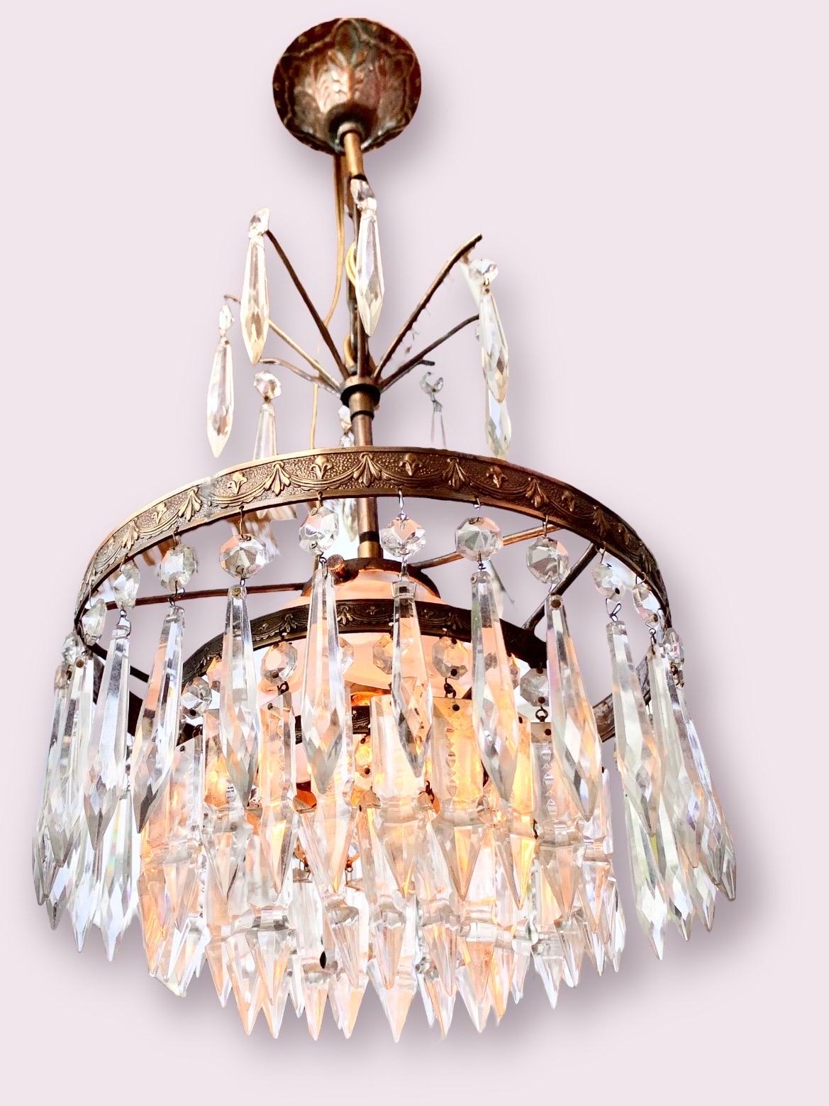 An Art Deco tiered crystal, brass and iron chandelier with a central hand made frosted glass flower shade with one light. The two brass rings having a lovely swag and fleur-de-lis design.

This Is a petite chandelier that would be well suited for a
