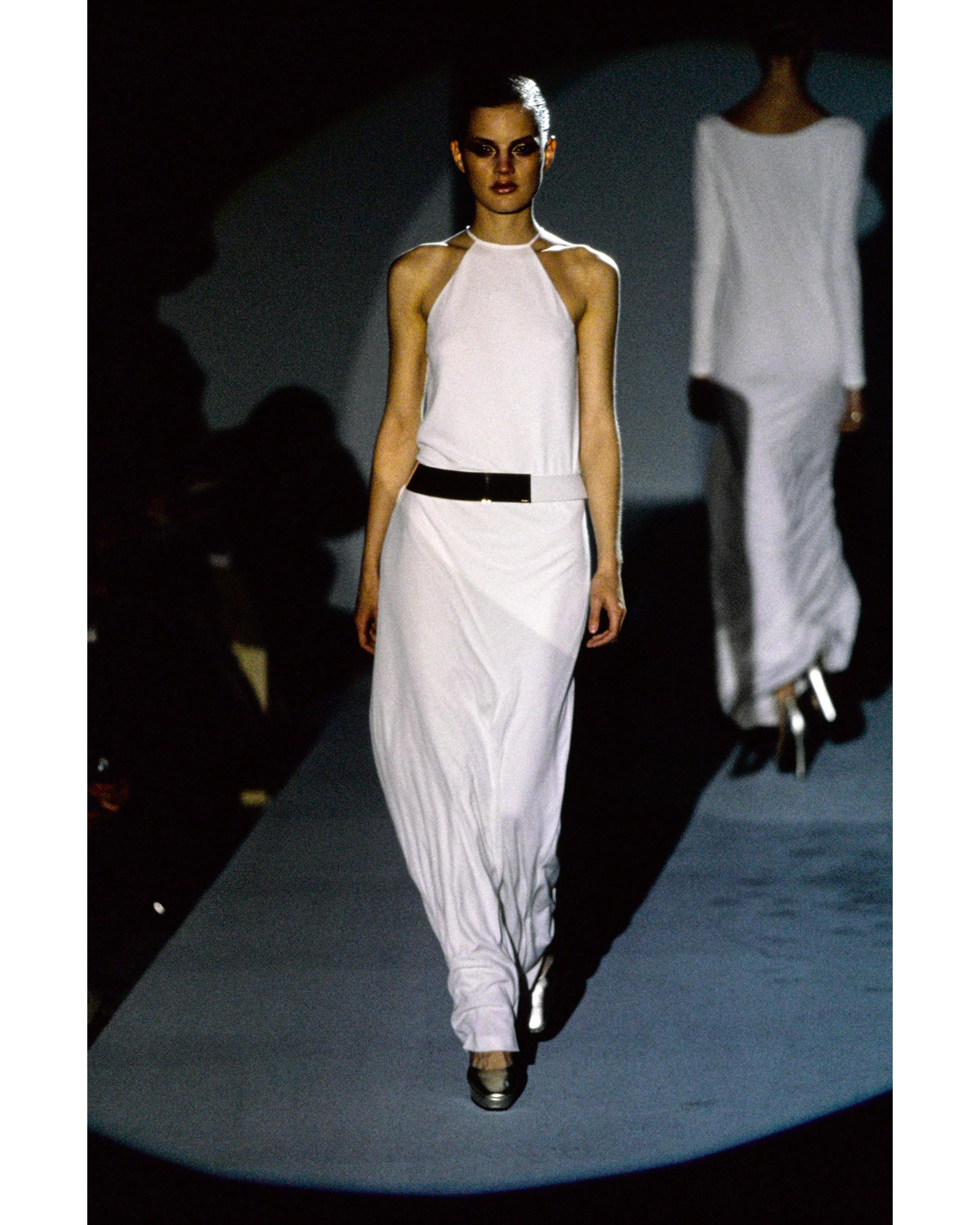 A/W 1996 Gucci by Tom Ford white gown with curved gold belt. White sleeveless halter neck gown with keyhole back cutout. Removable curved belt can be styled together or separately; on runway styled with belt partially on interior of dress, wrapped