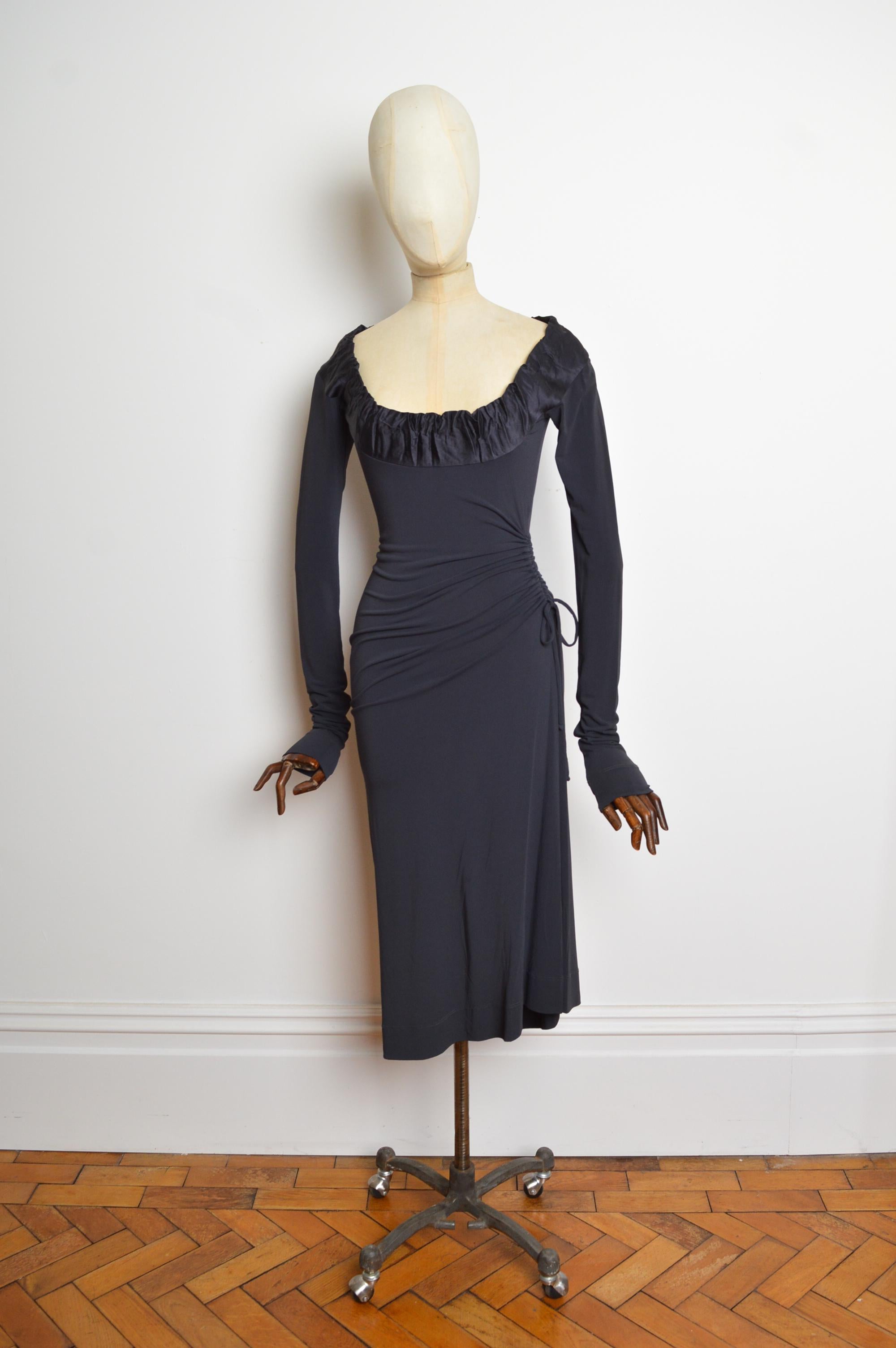 Abito Vivienne Westwood autunno/inverno 2004 in jersey nero elasticizzato, con maniche lunghe, scollatura a palloncino e orlo midi. Il taglio è caratterizzato da un dettaglio increspato superbamente lusinghiero e regolabile in vita. 
Taglia