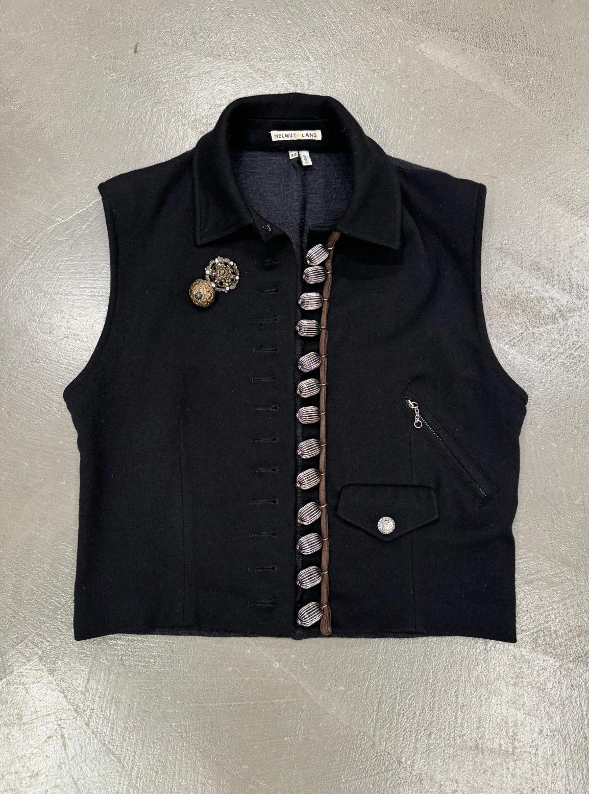 Gilet in lana con gingilli in metallo per la sfilata Helmut Lang A/W1989

Questo raro gilet di Helmut Lang della collezione autunno/inverno 1989 esemplifica la maestria dello stilista nella decostruzione e nei dettagli industriali. Realizzata in