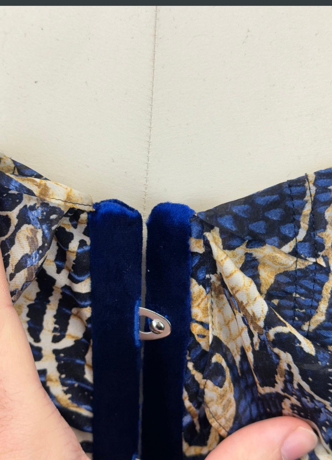 This stunning Roberto Cavalli corset from the 2005 collection embodies a bold and eclectic aesthetic. Crafted from a luxurious blend of rich velvet and silk, the corset features a striking print that combines ornate baroque patterns with animal