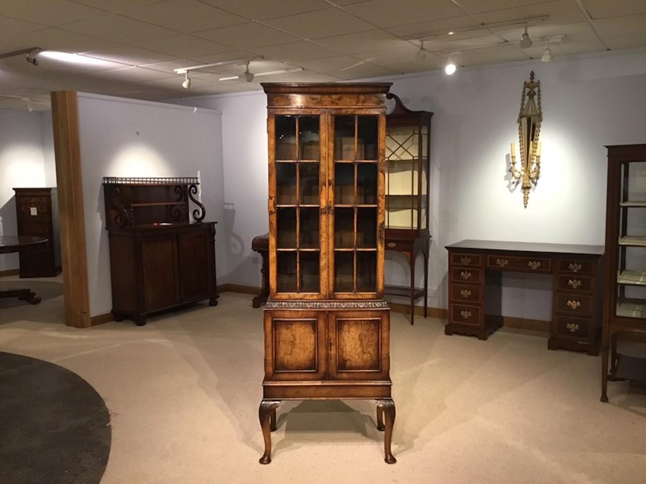 A walnut George I style bookcase by Maple & Co. The upper section veneered in burr walnut with moulded glazing bars and opening to reveal three adjustable oak shelves. The lower section having an acanthus carved frieze above twin walnut veneered