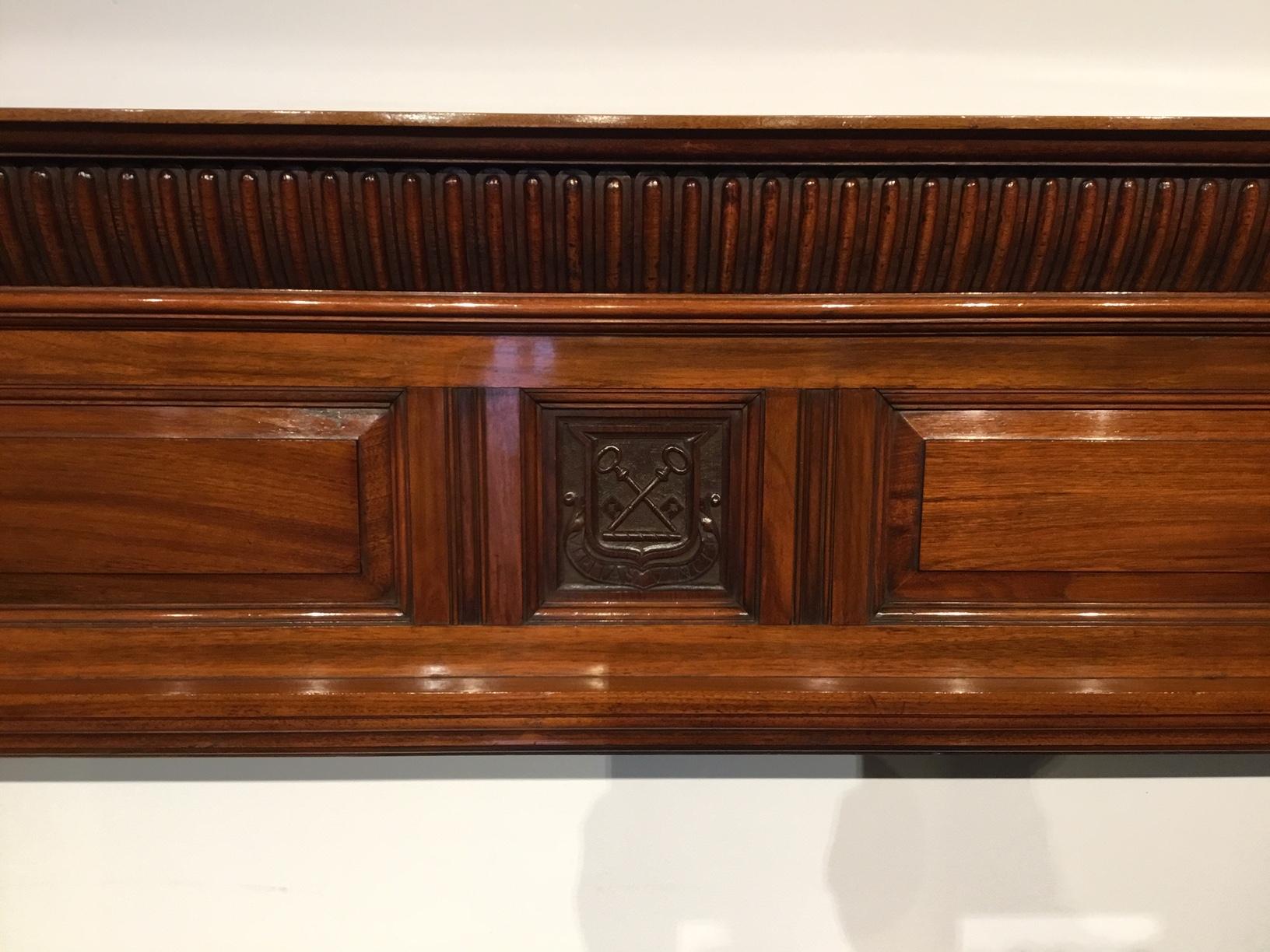A walnut late Victorian period antique fire surround. The solid walnut top with a gadrooned and carved frieze above the central rectangular paneled section, having a finely carved coat of arms with a Latin inscription and cross keys motif. The