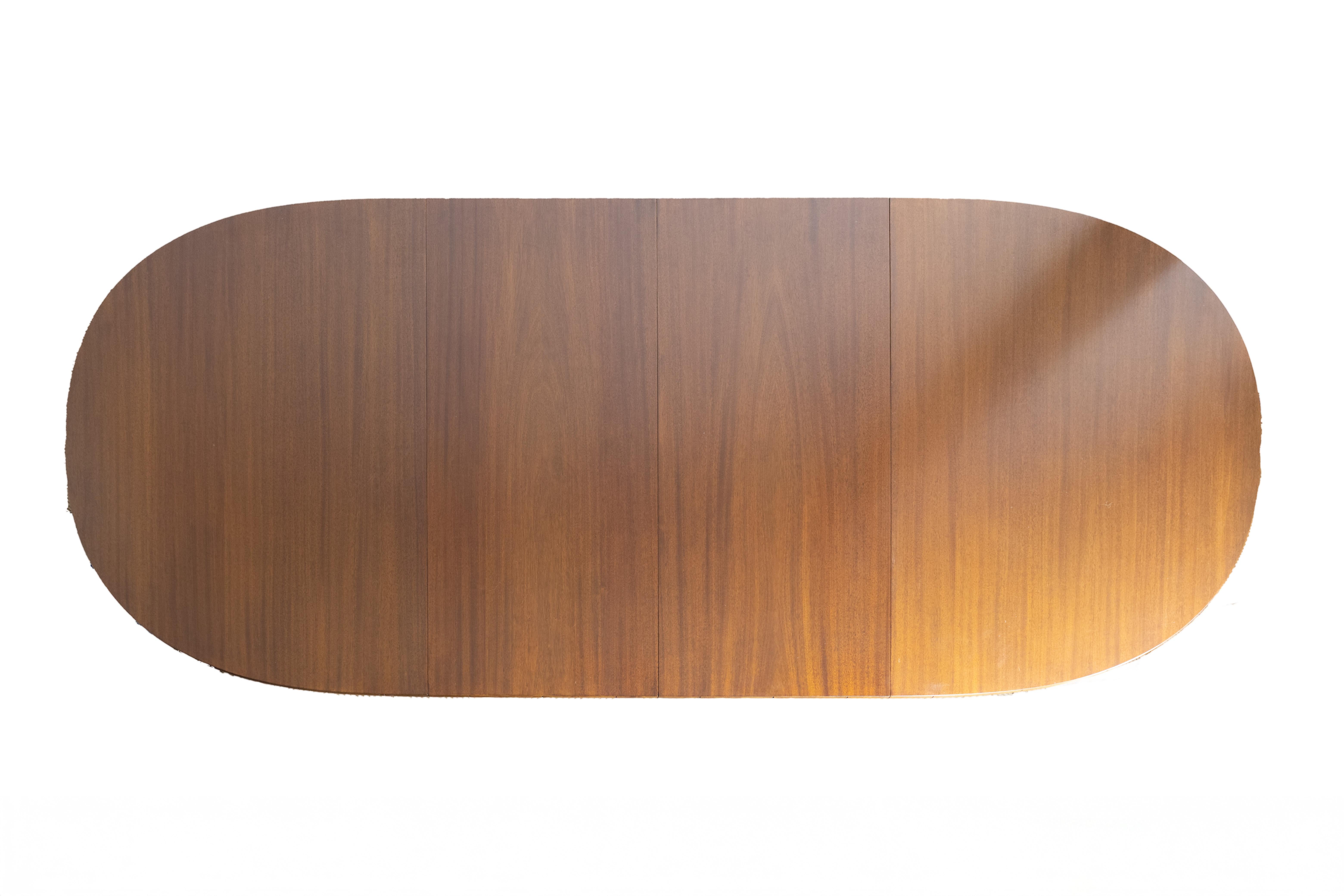 An oval dining table in the English Regency style featuring a walnut top and matching solid walnut extension leaves. The table stands on six round, tapered legs, each detailed with carved faux bamboo turnings. Additional faux bamboo elements accent