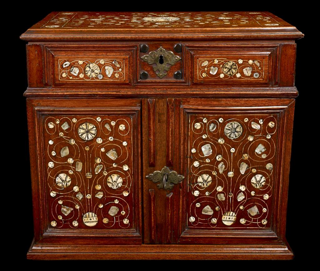 A walnut table cabinet, English, circa 1670, profuse mother of pearl and bone decoration to the doors and the top lid; the doors open to reveal an arrangement of 8 draws, the cabinet measures 21 ½ inches wide, 18 ½ inches tall and 14 inches