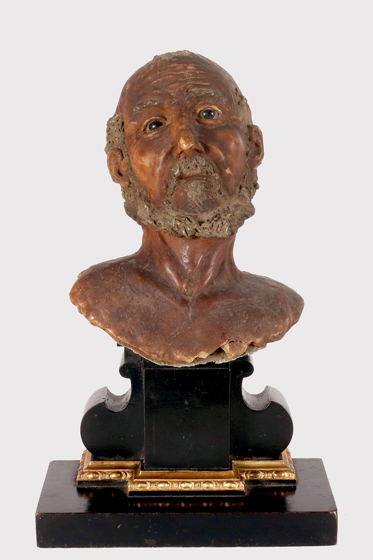 Una scultura in cera (modellazione in cera) del busto di un Santo.
La scultura è montata su una base in legno di frutto ebanizzato, con una base rettangolare, con una parte in rilievo evidenziata da una decorazione in legno intagliato e dorato con