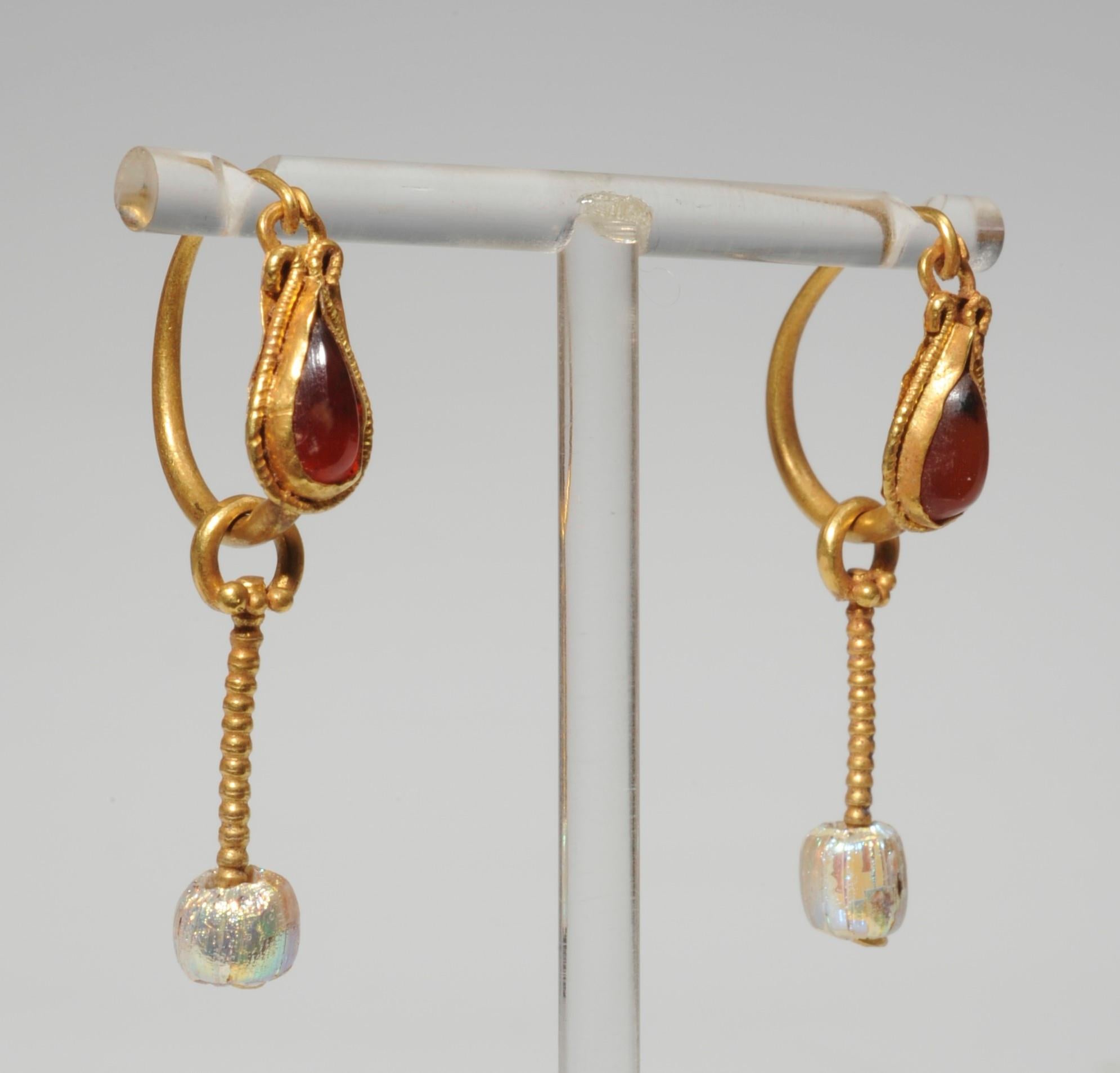 A pair of precious golden bow-earrings. The box of the drop shaped carnelian inlay is surrounded with a twisted wire that ends at the top into a volute and a little ring. From a small ring decorated with three globules hangs a bobble into which a