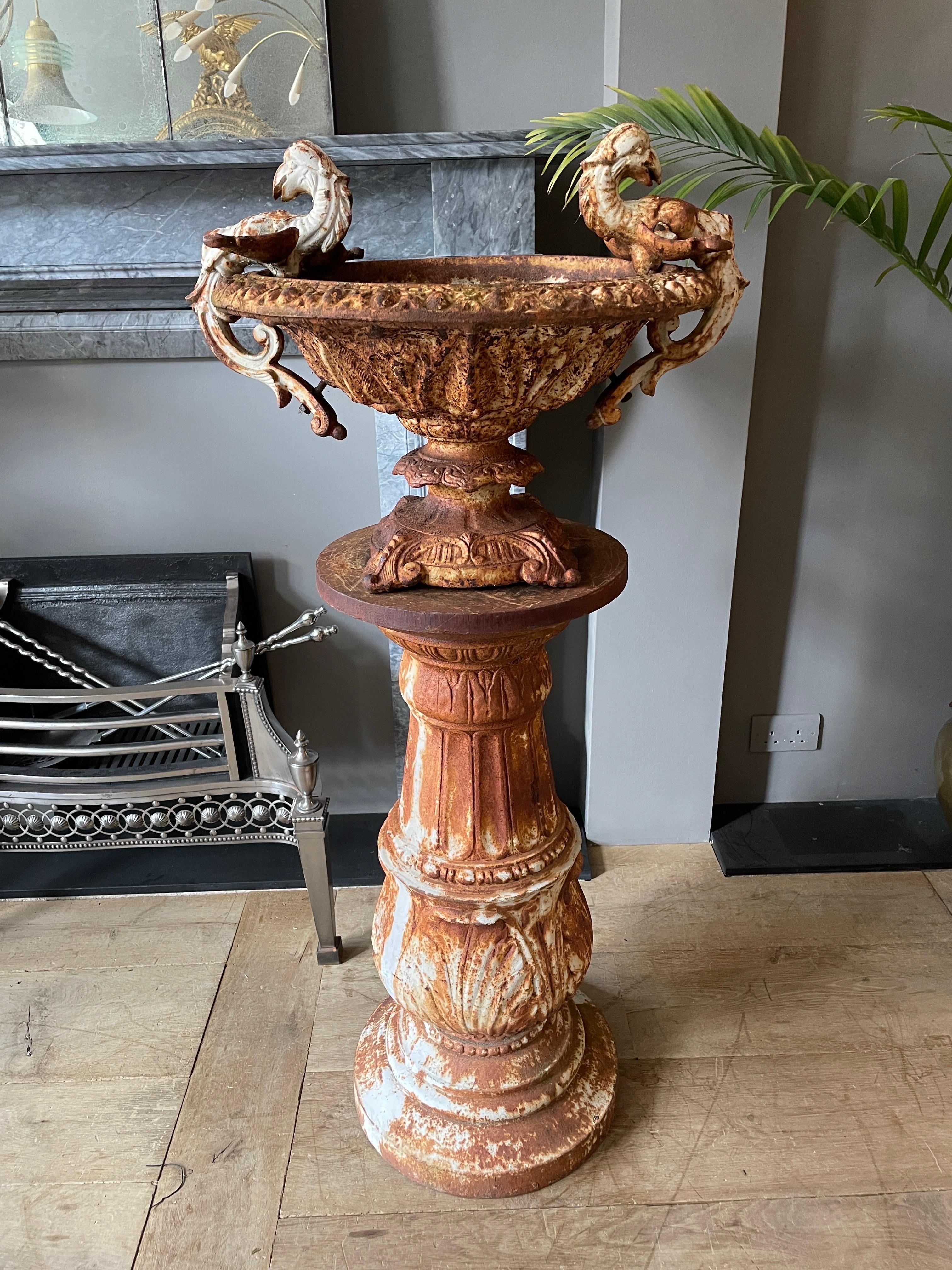 A weathered cast iron urn and pedestal. The urn with classical mythology creatures, foliate scrolled feet, egg and dart rim. The pedestal with circular socle base, baluster support with beading, fluting and egg and dart casting. Great warm patina.