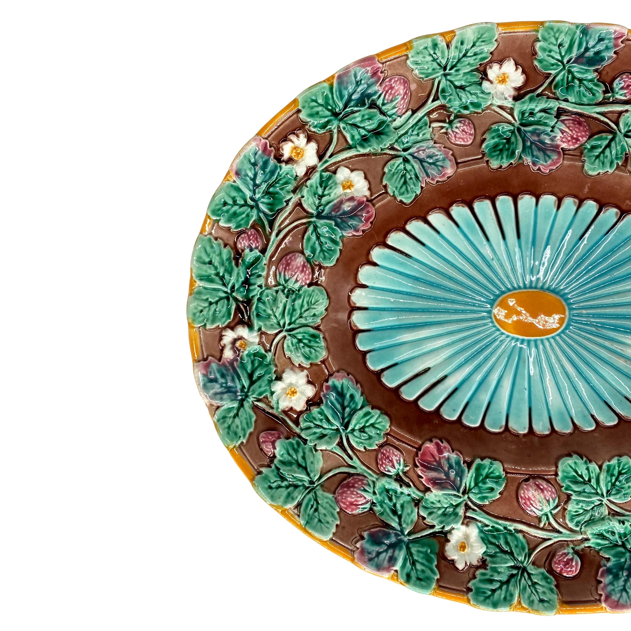 Un piatto ovale in maiolica di Wedgwood da 13 pollici modellato con una fascia continua di fragole smaltate in rosso e una vite fiorita smaltata in verde, il pozzo con un  fiore stilizzato smaltato in turchese e ocra, il rovescio con i marchi