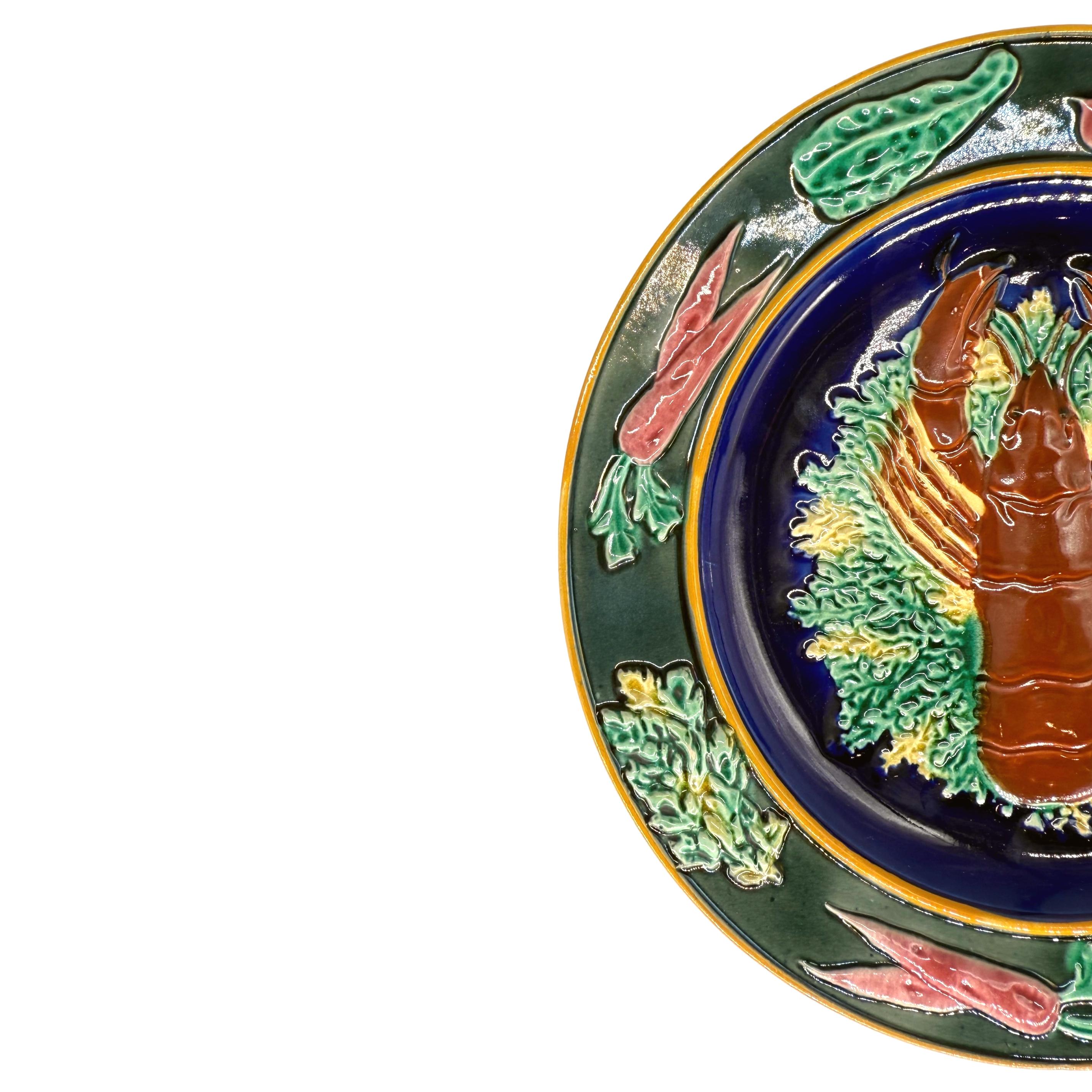 A Wedgwood Majolica Lobster Plate, with the central figure of a red-glazed lobster on sea greens on a cobalt blue ground, and with relief molded root vegetables to the lip, the reverse with impressed marks: WEDGWOOD and three letter date code (K for