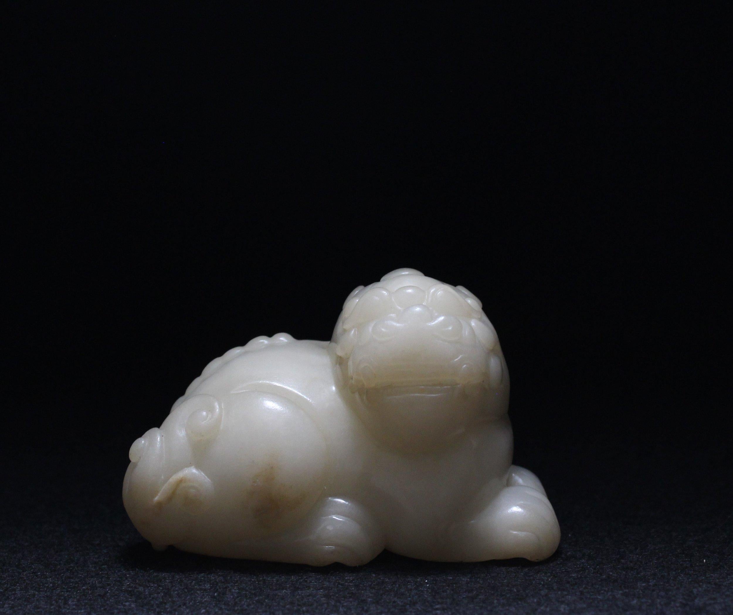 This recumbent white jade beast has its large head turned to one side.  

The creature has large, tear-drop-shaped, bulging eyes framed by curling-down eyebrows. Notably, there is a half-dome extrusion representing a third eye positioned between the