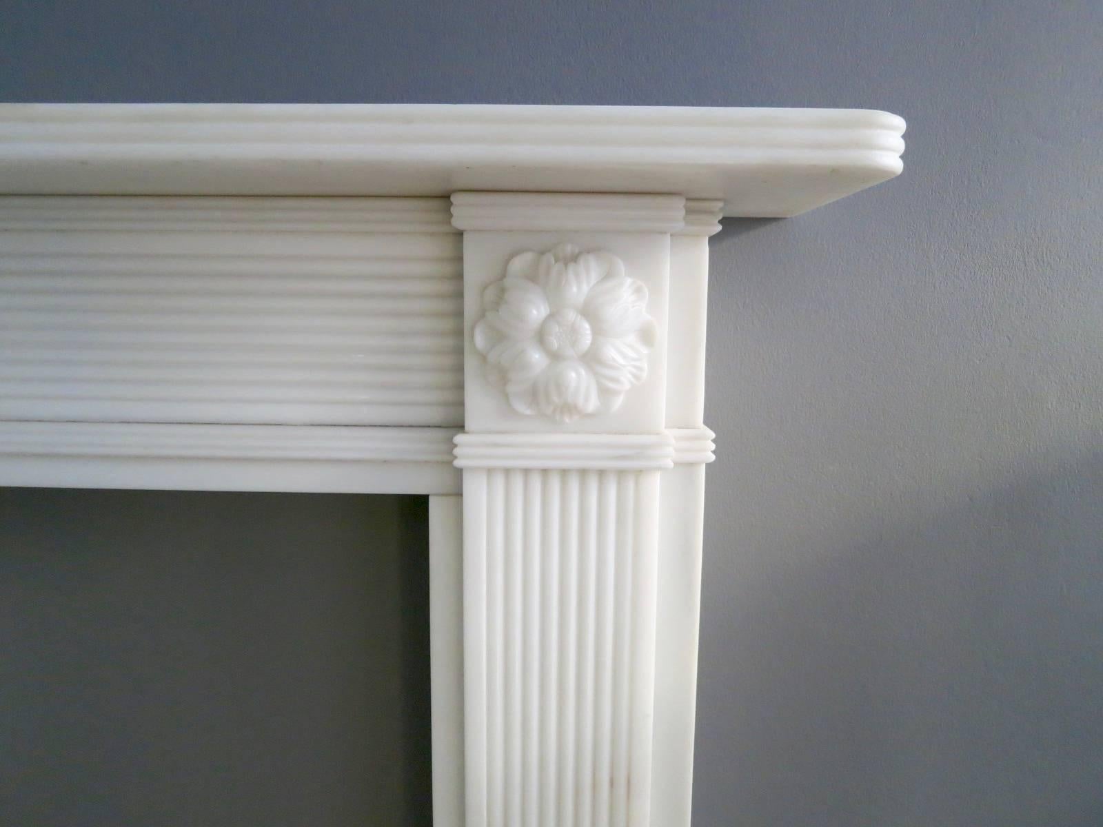 A good quality copy of an earlier piece from our antique catalogue. The reeded jambs surmounted by carved rosettes with a conforming reeded frieze. The mantel being double reeded to match. This Regency style surround has been lightly aged.