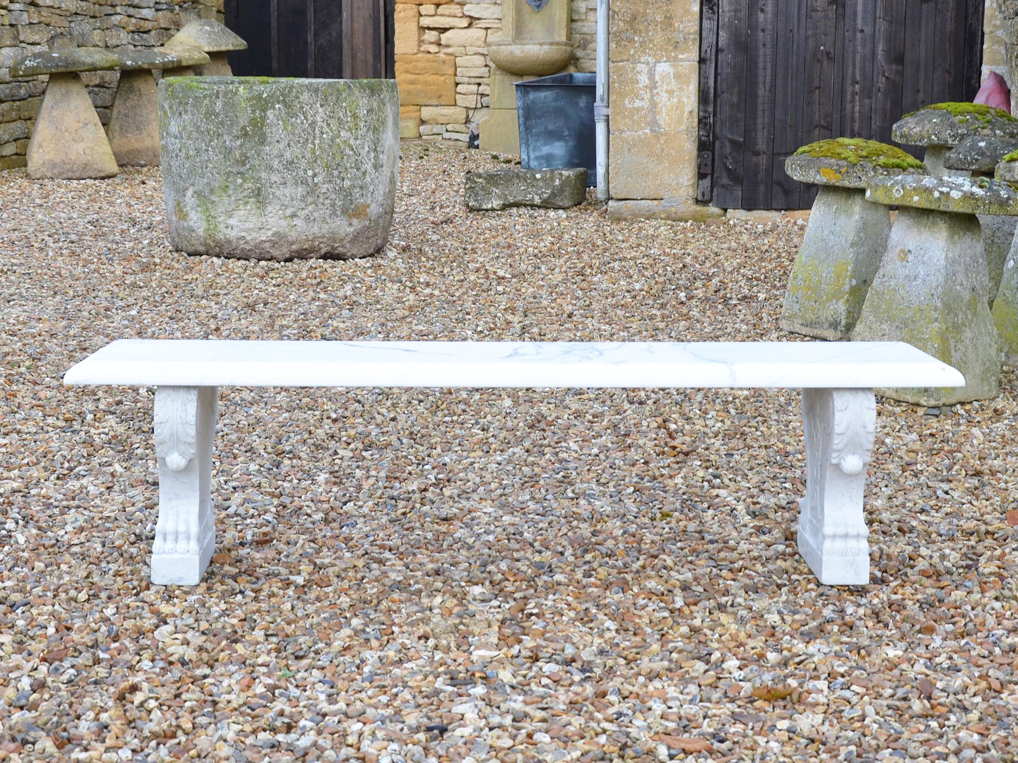 A white marble garden bench raised upon cabriole leg supports, having acanthus leaf decoration.