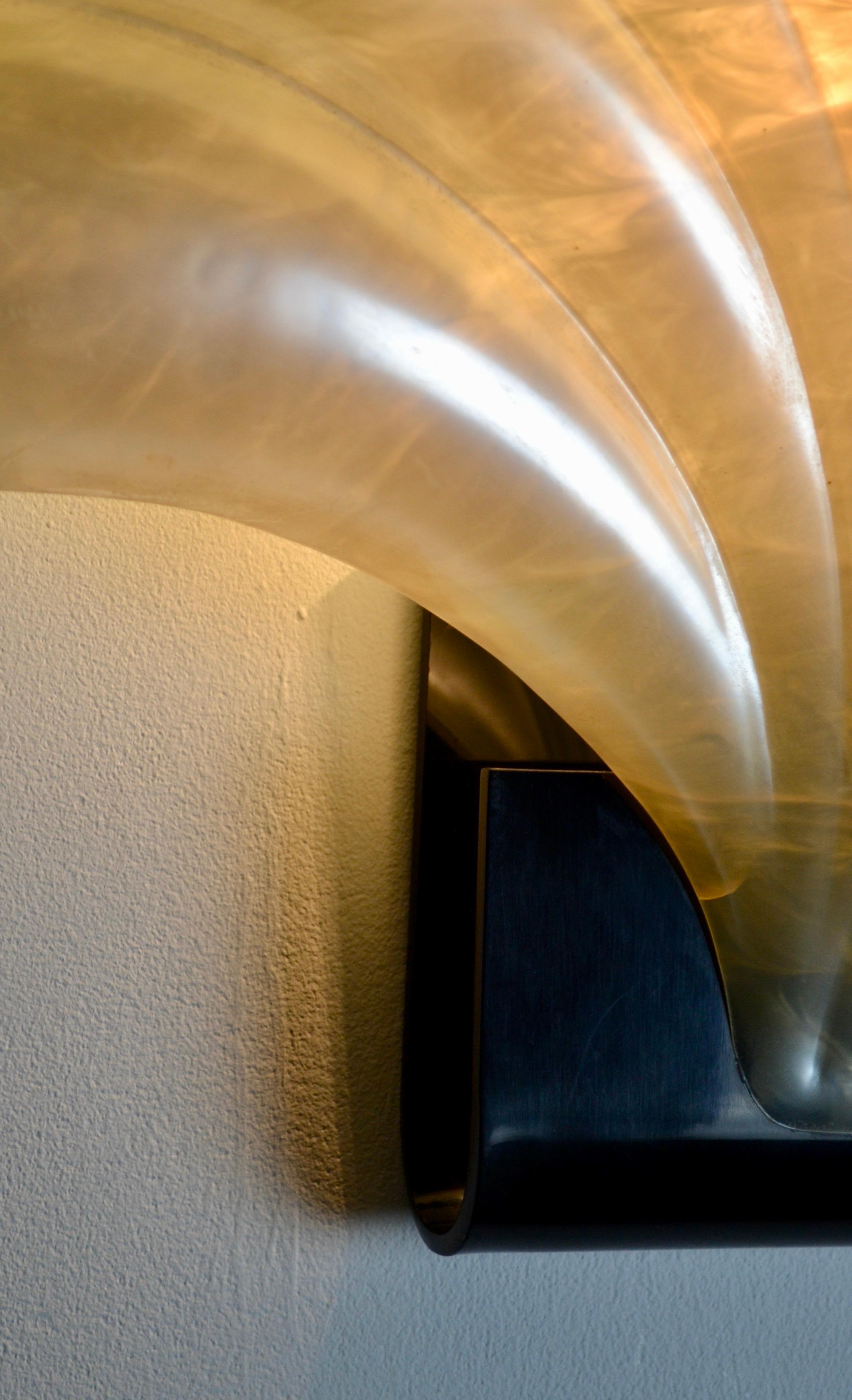 This 1970s wall lamp, designed by the renowned French designer Roger Rougier, stands out for its elegant and sculptural aesthetic. Made of translucent acrylic, it takes the shape of a shell, evoking the delicate curves of nature. The light, subtly