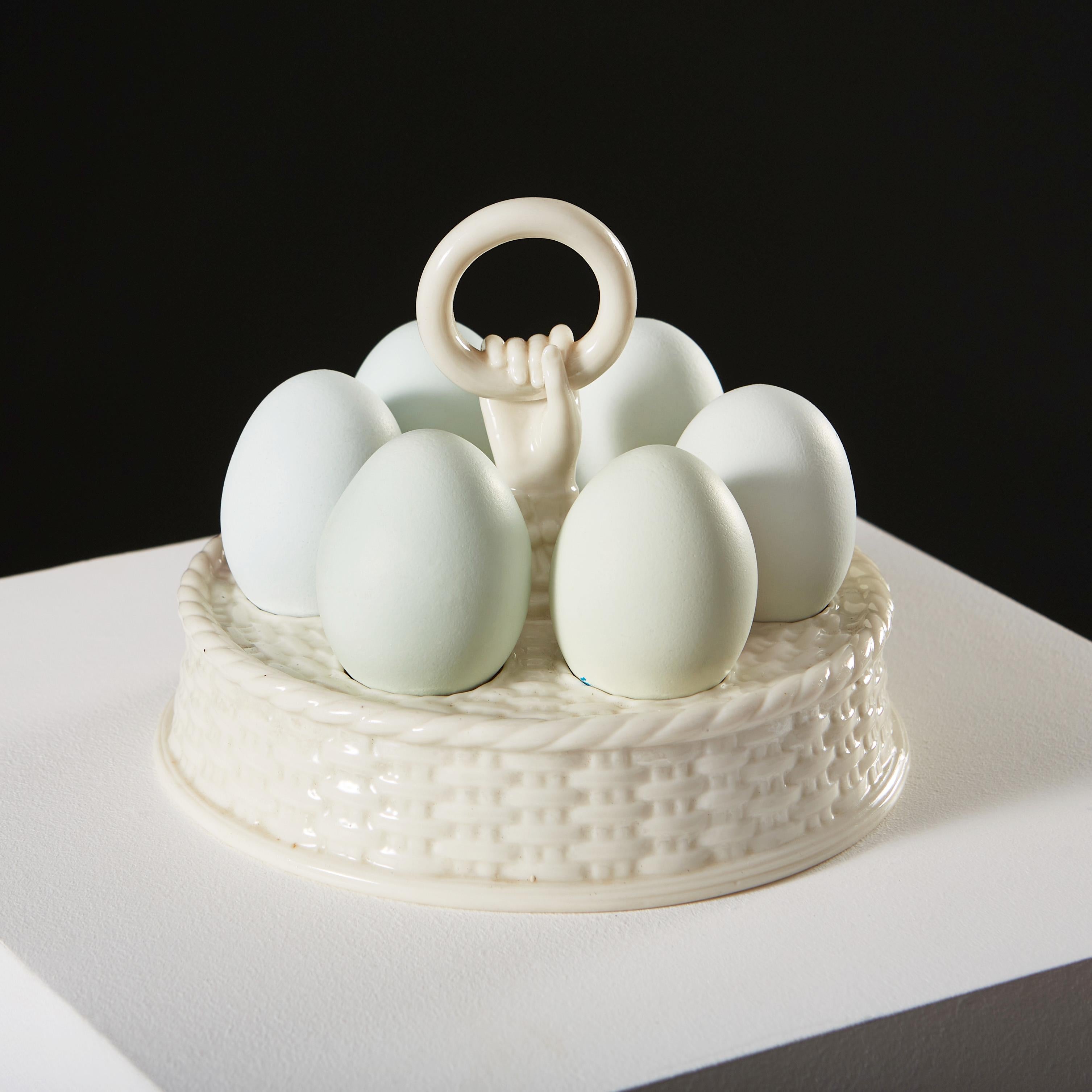 An early twentieth century egg holder for six eggs, with basket weave decoration to the sides and top, with protruding hand and ring to the centre.