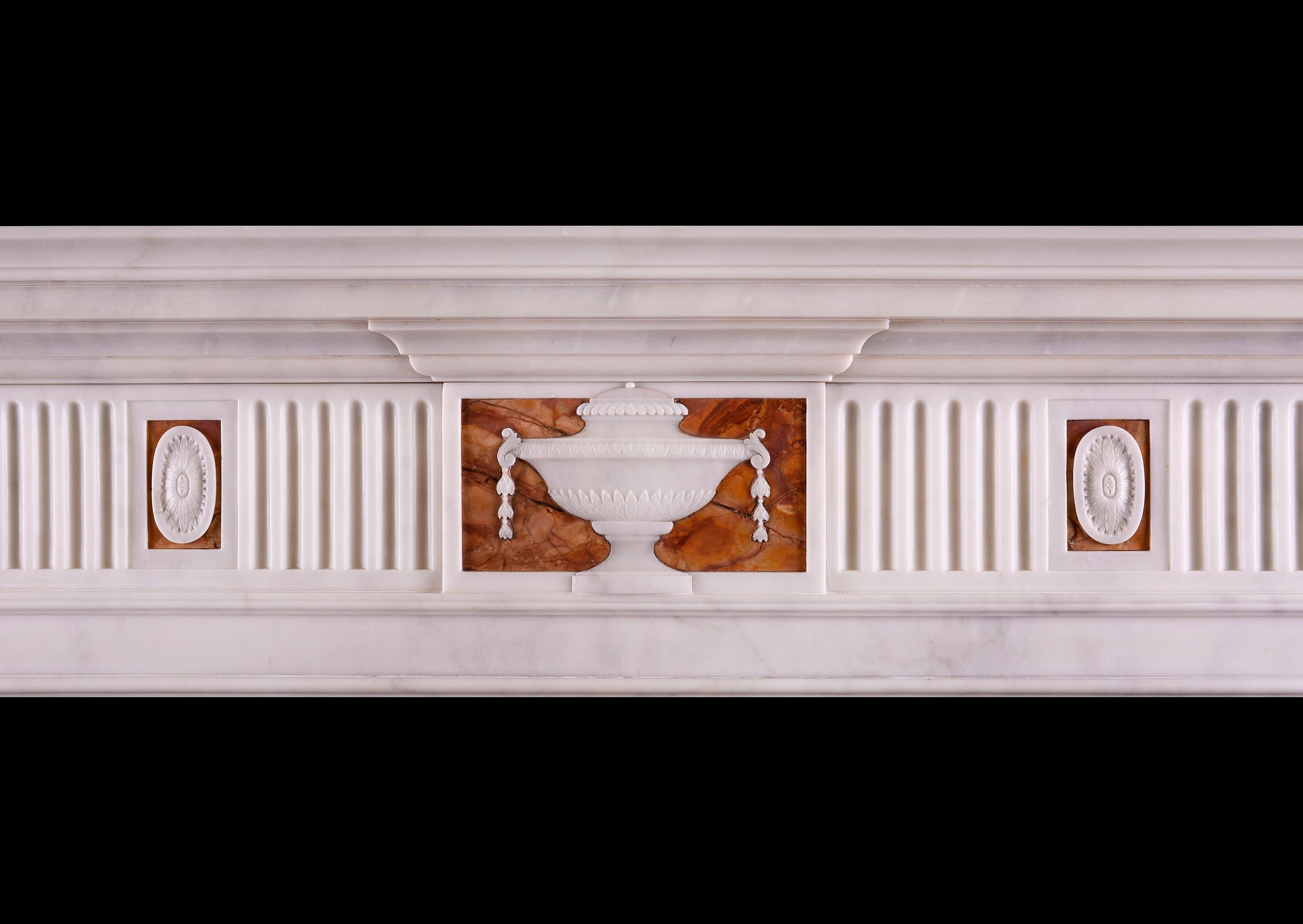 A white Statuary marble fireplace with Jasper inlay in the late Georgian manner. The fluted frieze interspersed with carved paterae, with carved urn to centre. The jambs with carved acanthus leaves above plinths, surmounted by inlaid flutes on