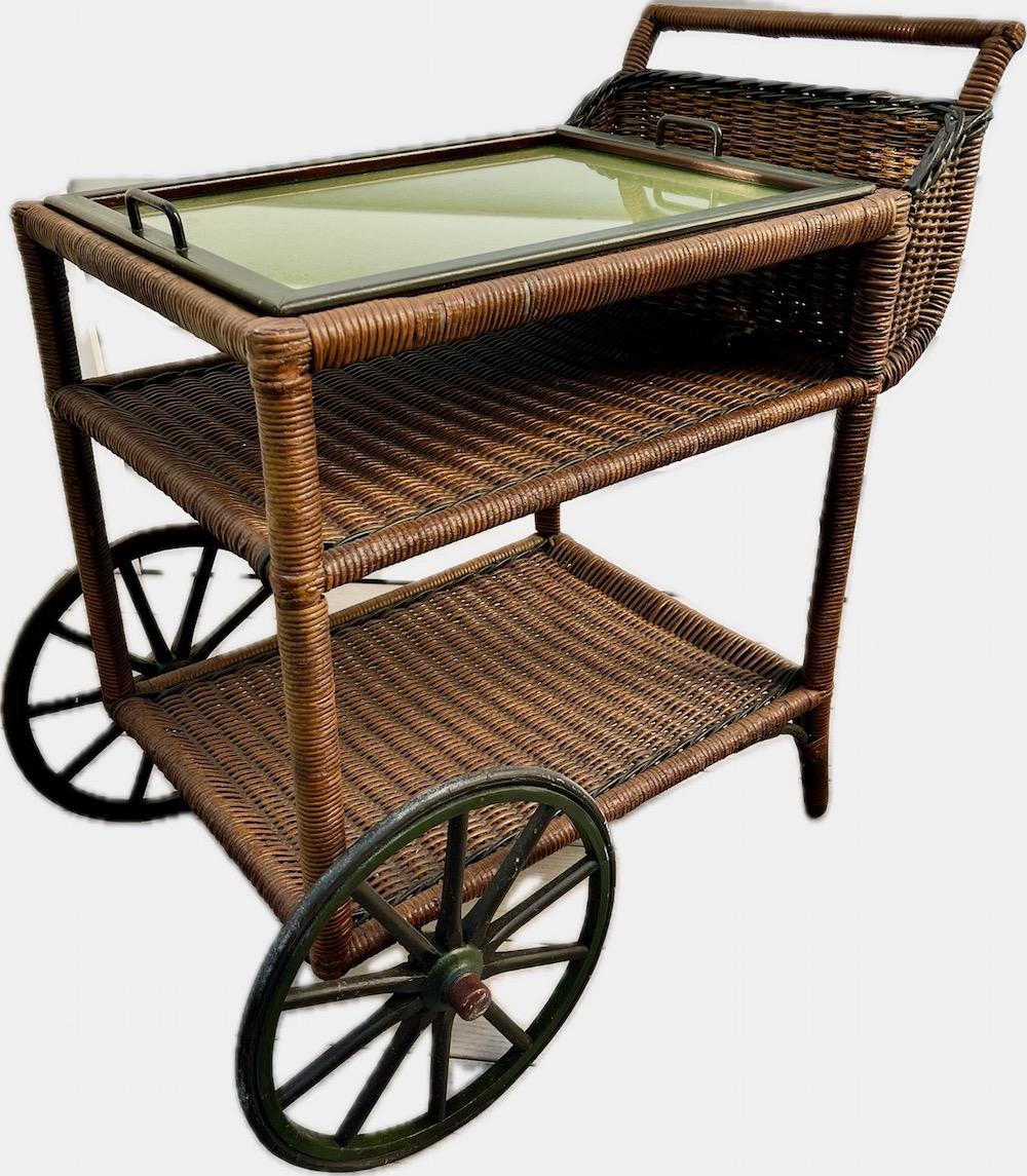 This is a vey unique Antique Wicker Tea / Bar Cart in natural finish with colored dark red, black and green trim, American, C.1910.
This handsome serving cart is unique in its style. I have never seen this design before on a serving cart. The reed