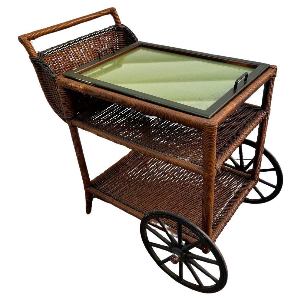 Un carrito de mimbre para té o bar con bandeja para servir, estante central e inferior y cesta para botellas