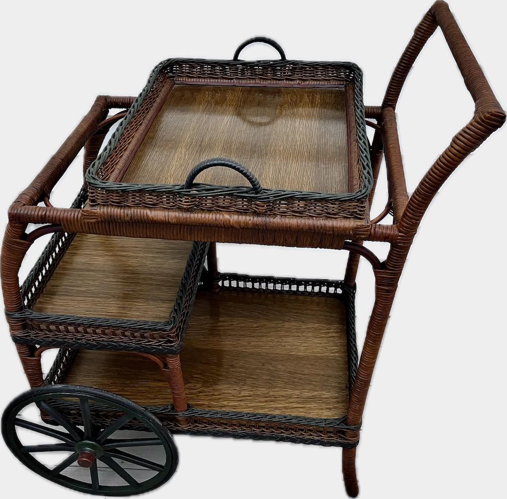 A beautiful Antique Wicker Tea / Bar Cart, American, C .1910 and designed in a natural finish with black and green accent trim which is used on both the carts braid trimming and wheels. The large removable top serving tray comes with a bar finish on