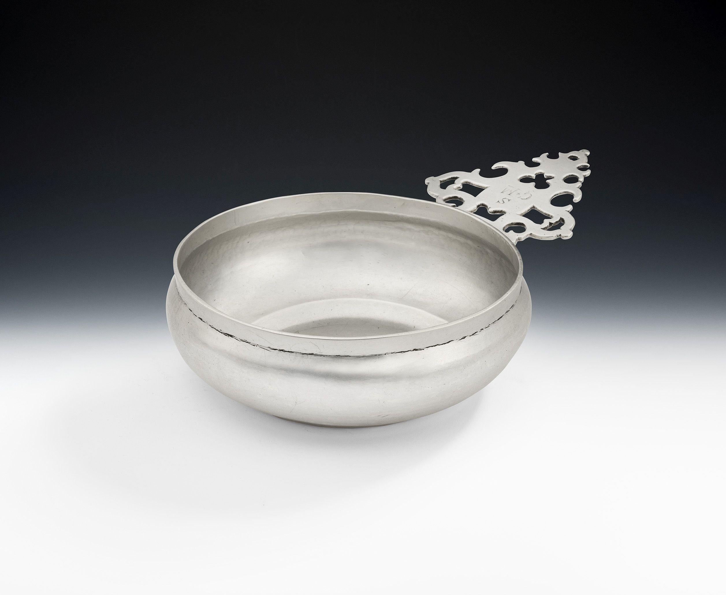 These side handled bowls were almost certainly used as eating vessels. The bowl has circular baluster sides which rise to a straight rim. The cast handle is shaped and naively pierced with scroll work and stylised heart motifs. It is also engraved