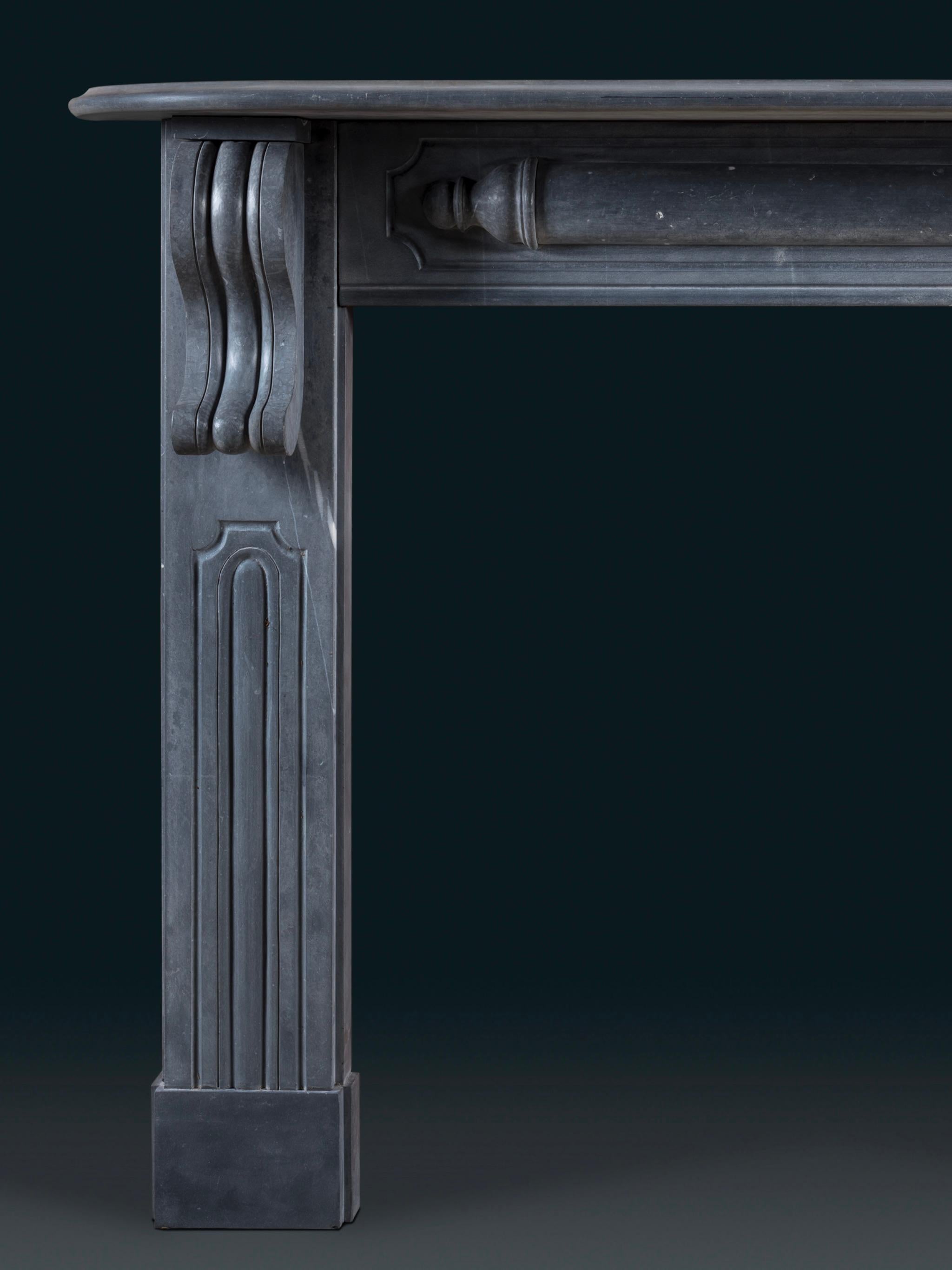 Cheminée de style Régence entièrement sculptée dans du calcaire bleu. Cette pièce présente de nombreuses caractéristiques inhabituelles et ludiques. Les panneaux à champs qui ornent les jambages s'arrêtent en rencontrant les robustes blocs de pied.