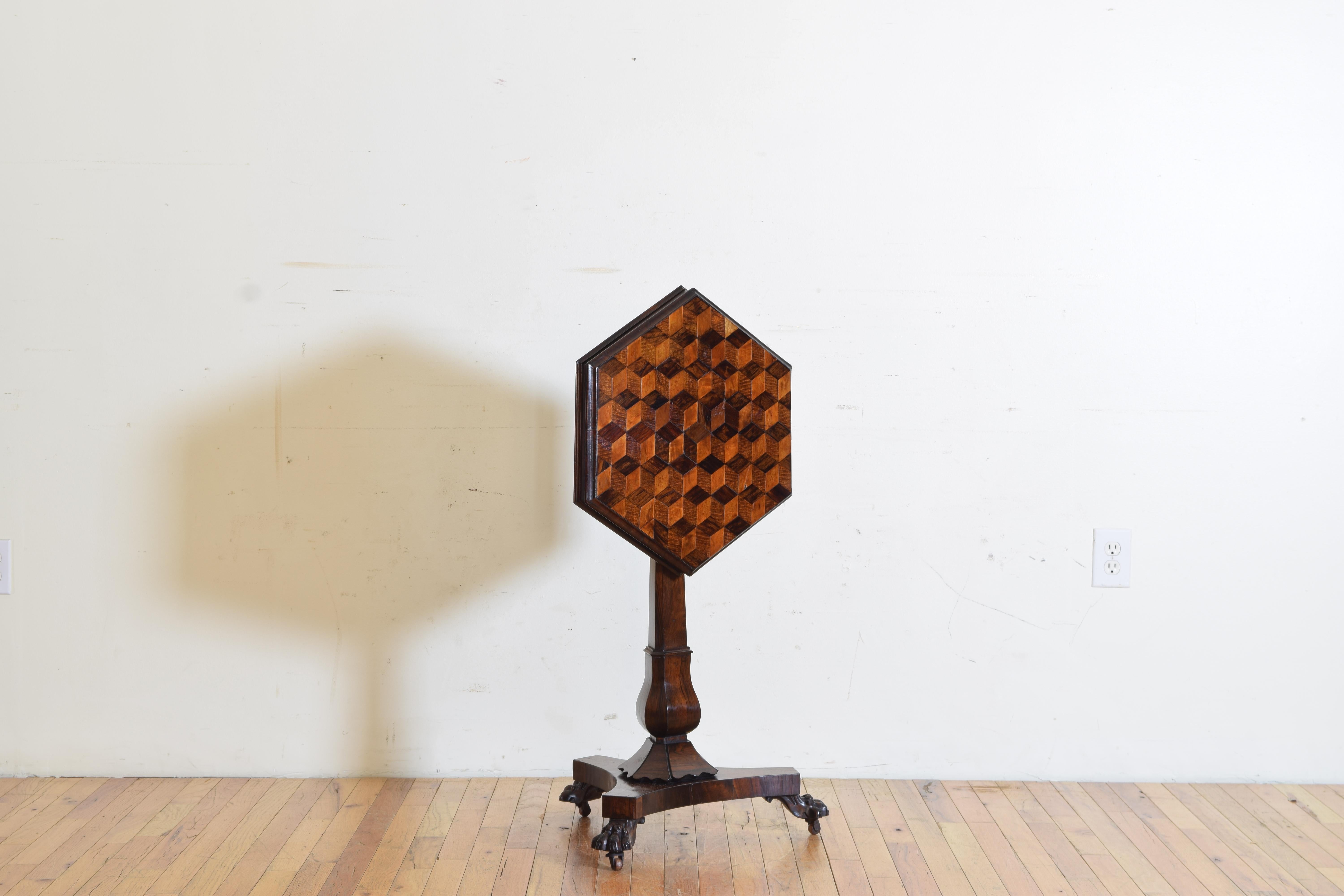 Having a hexagonal top with parquetry patterned veneers with molded apron, the top tilting to vertical, raised on a three sided shaped standard resting on a tripartite base resting on carved and ebonized paw feet, Provenance: Bonhams, Los Angeles,