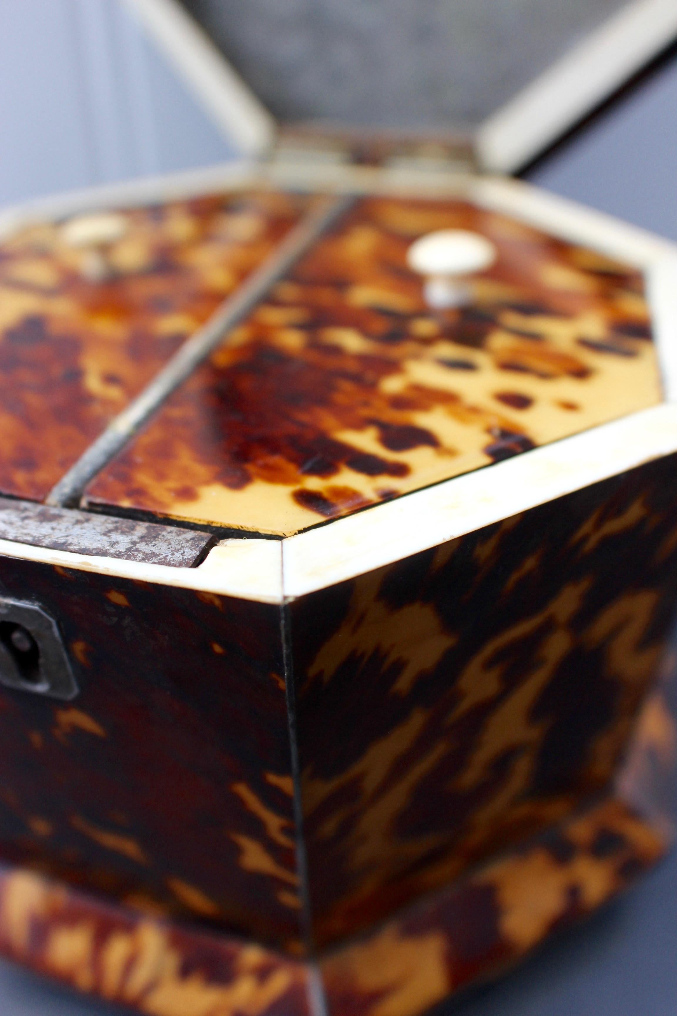 A William IV tortoiseshell and ivory veneered tea caddy, circa 1840. Octagonal shape, the lid with sloping sides, flat top fitted with knop finial, the interior with two lidded compartments.
  