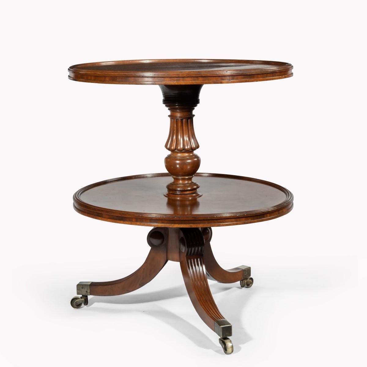 A William IV two tier mahogany table attribruted to Gillows, with two circular shelves, the top one with a dished edge, supported on a reeded and turned baluster column, all on three splayed reeded legs with brass caps and castors. English, circa