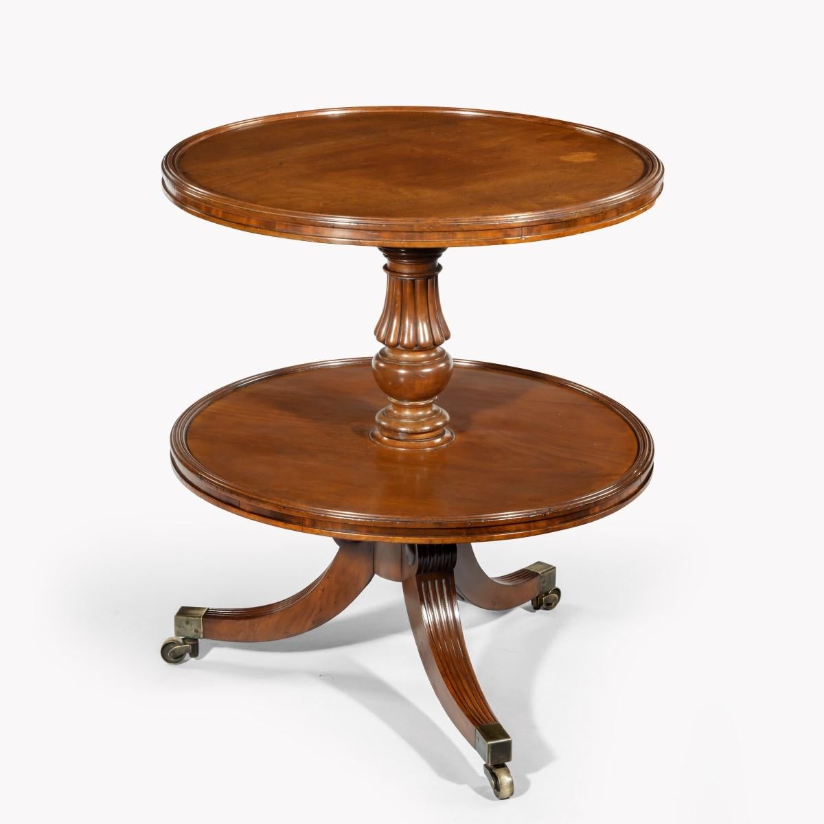 A William IV two tier mahogany table attribruted to Gillows, with two circular shelves, the top one with a dished edge, supported on a reeded and turned baluster column with two flanges, all on three splayed reeded legs with brass caps and castors.