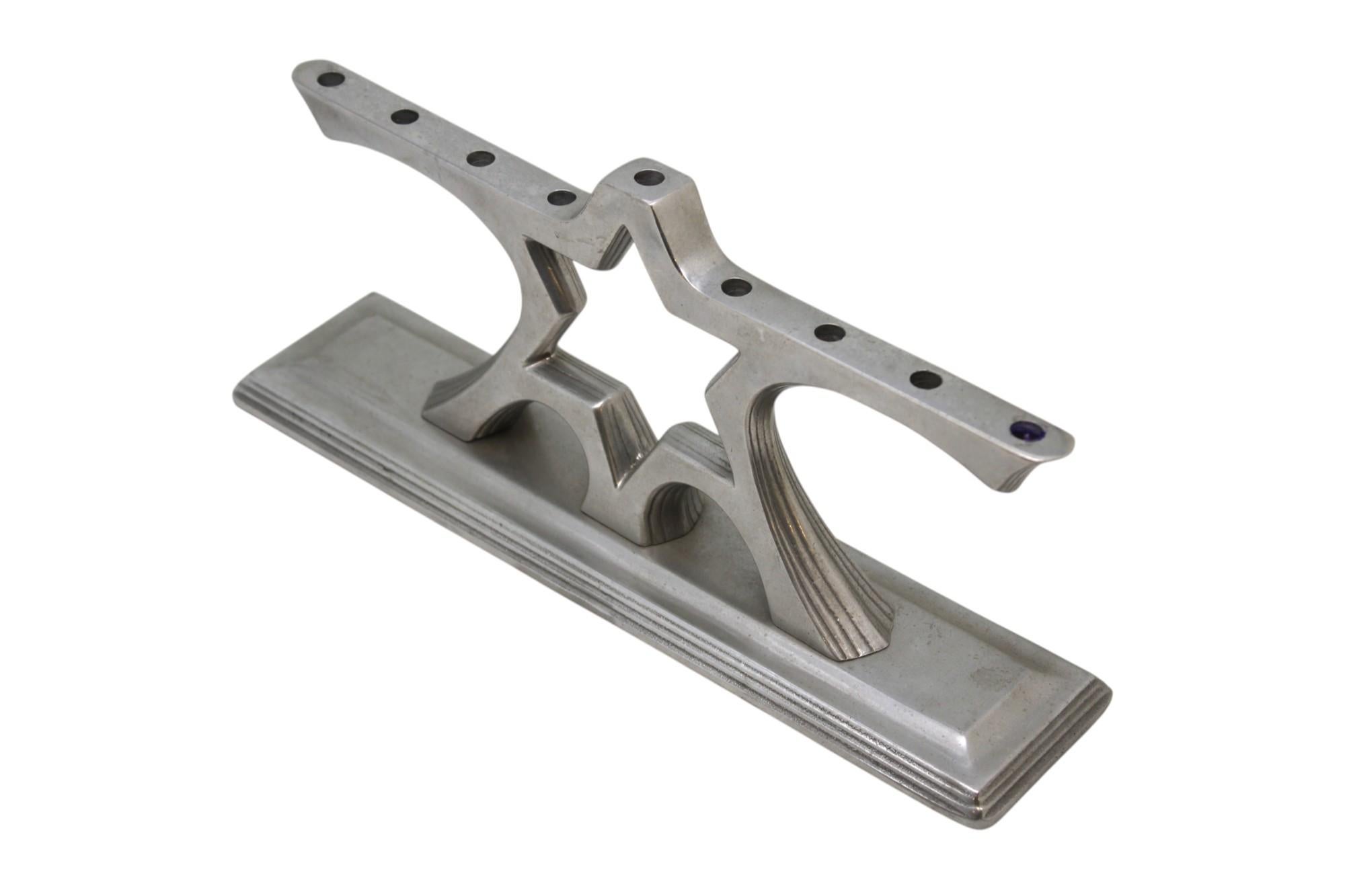 Questa lampada scultorea per Hanukkah, realizzata da Wilton Armetale, è realizzata in lega di alluminio fuso, nota per la sua durata e la sua lucentezza argentea. La menorah poggia su una base rettangolare a gradini, che fornisce un solido supporto