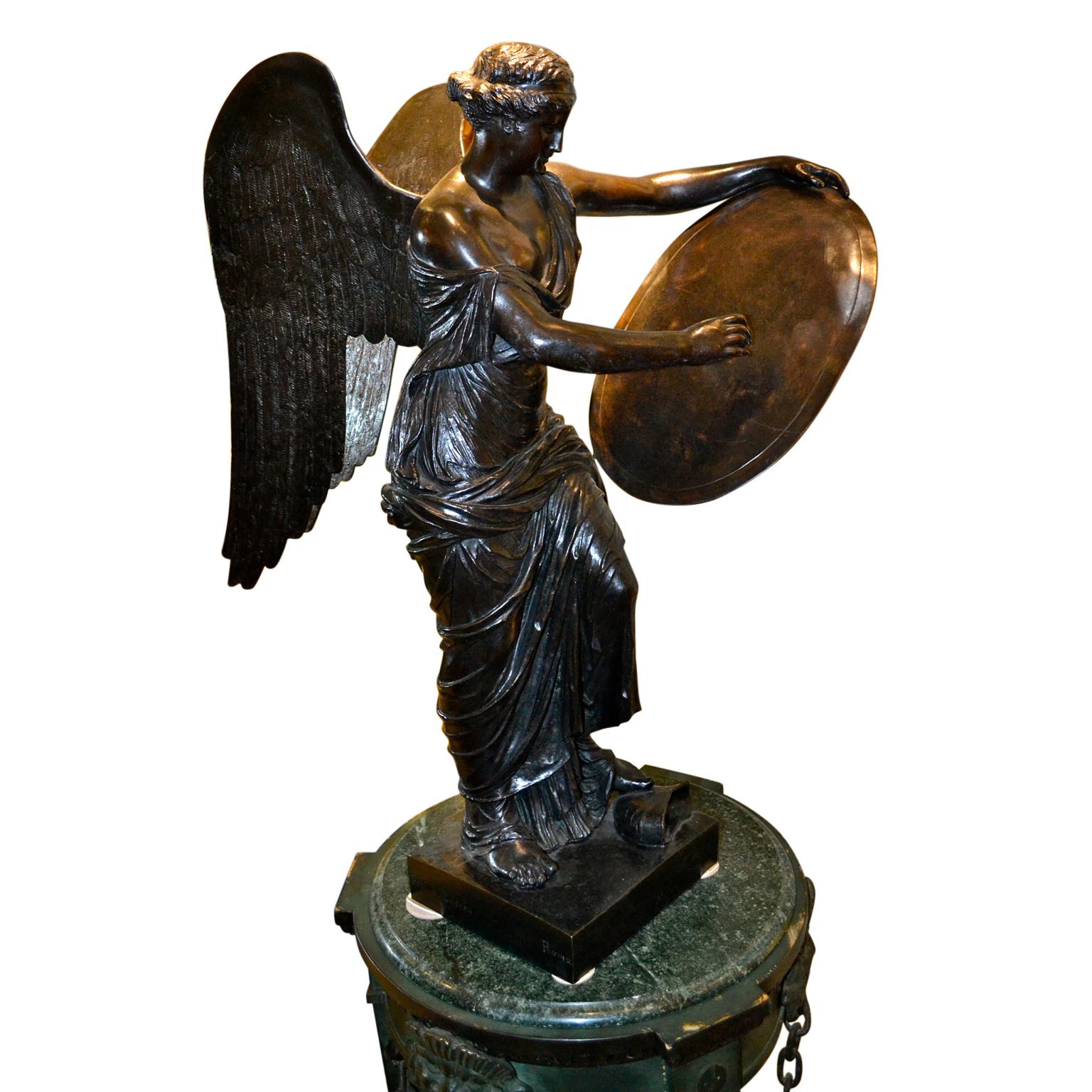 A large well cast black patinated bronze statue of a Greek winged Victory. She is partially draped and holds a shield shaped tablet in one hand and a writing instrument in the other. The base of the statue is inscribed Prof A Zocchi, Roma.