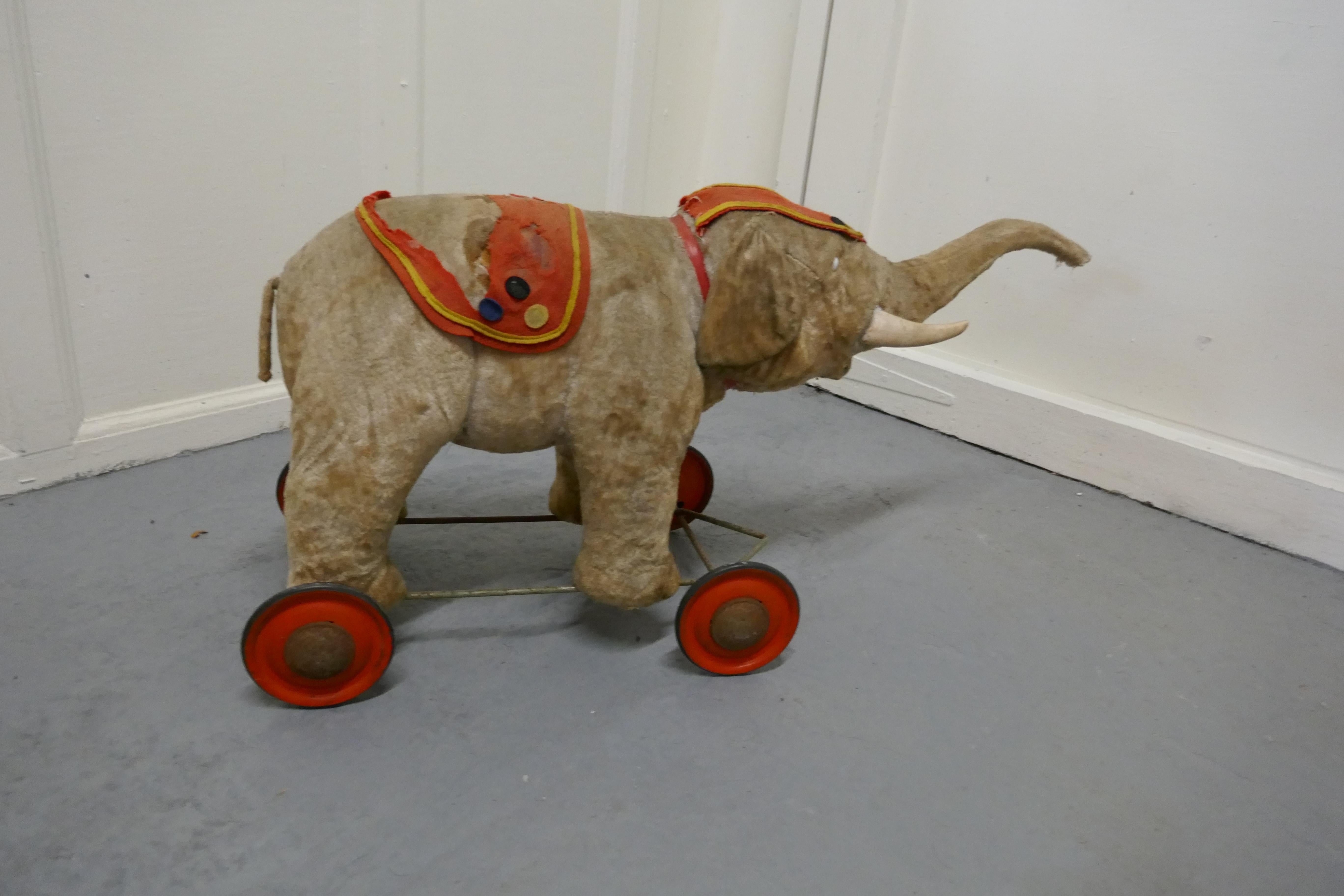 A wonderful Old French pull along circus elephant 

Our charming fellow has a a very worn felt coat/saddle and a matching head dress, he sits on red tin wheels , he has a delightful if rather frightened look from the eye


Used and Loved but