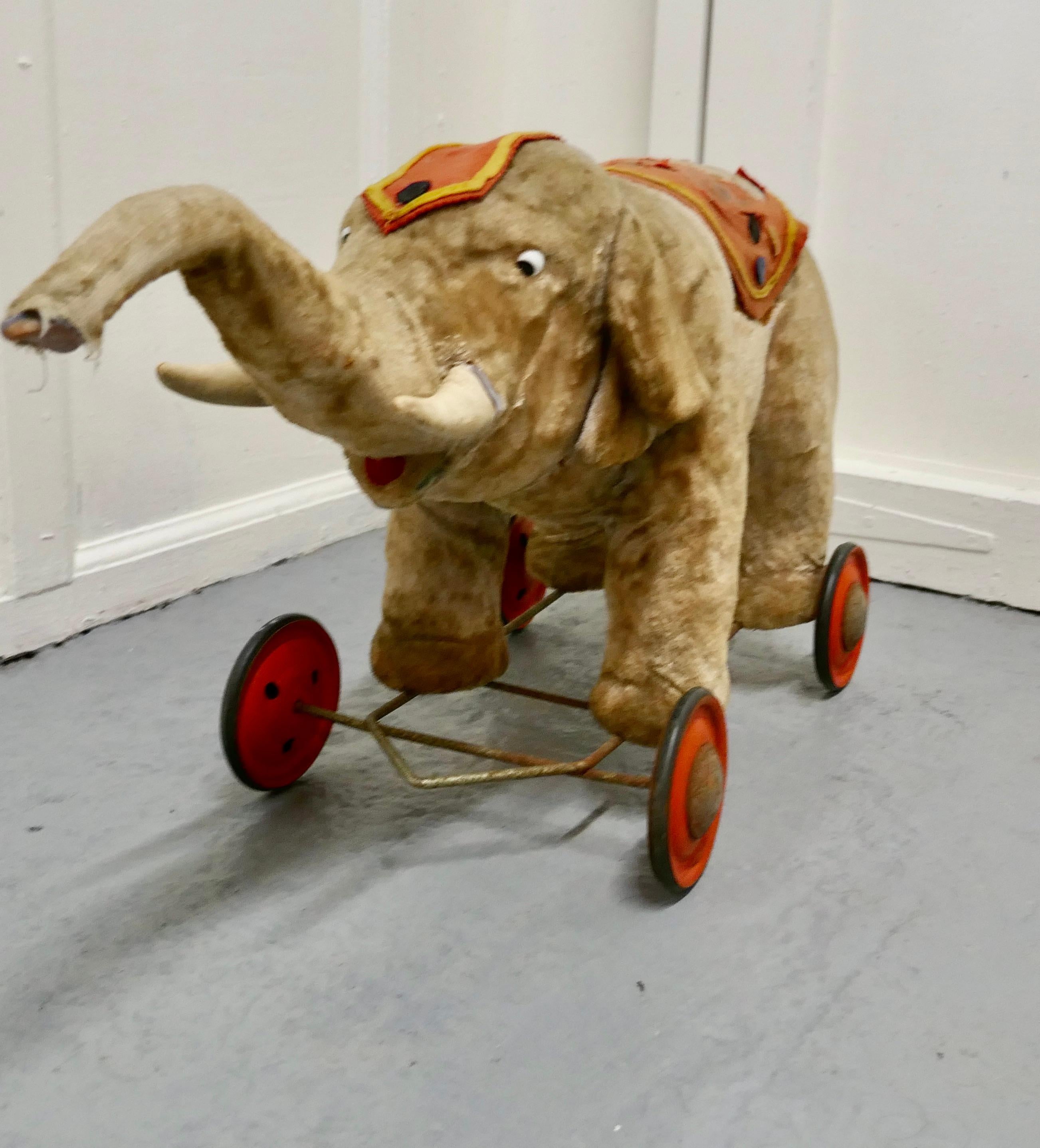 A Wonderful Old French Pull Along Circus Elephant 

Our charming fellow has a a very worn felt coat/saddle and a matching head dress, he sits on red tin wheels, he has a delightful if rather frightened look from the eye


Used and Loved but still in