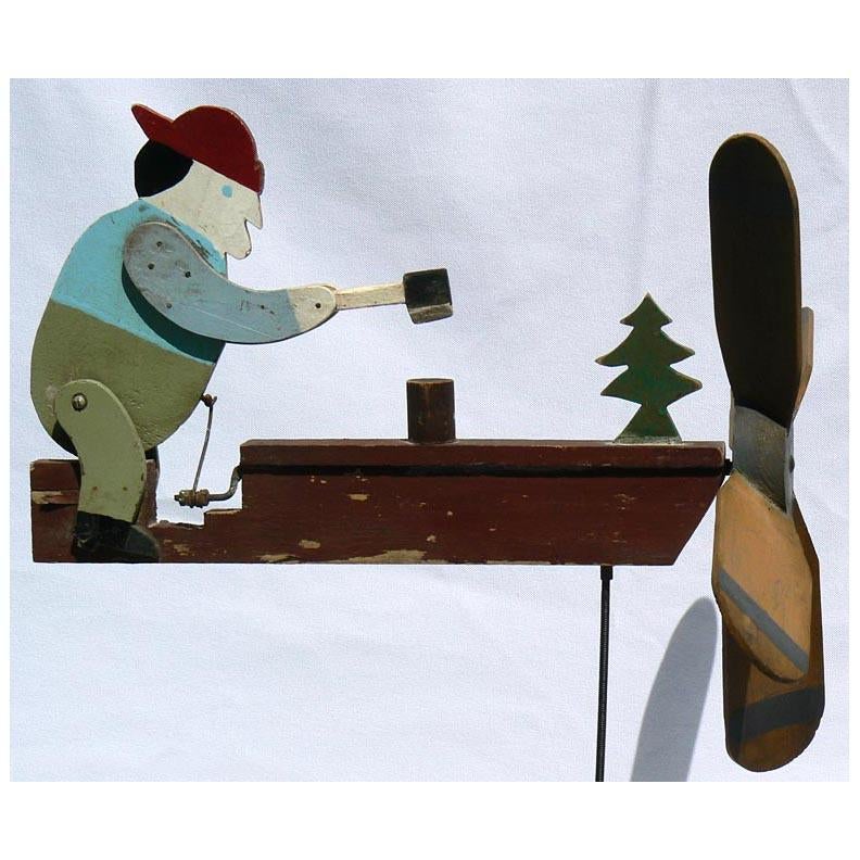 This is a woodchopper whirligig found in a barn in New Hampshire. The man, tree, and axe are made from pine, with plywood arms. The paint has good color with a bit of wear and has one or two small flakes present. This man stands 9 3/4