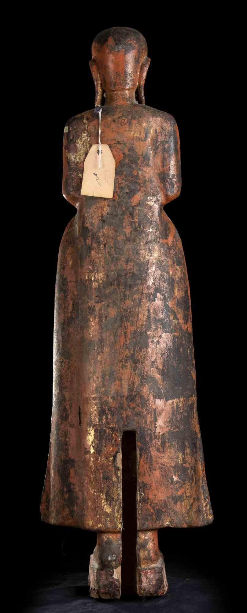 Eine weibliche Holzfigur.
Indien, 19. Jahrhundert.

Die Figur ist stehend dargestellt, mit zusammengelegten Füßen auf einem kleinen rechteckigen Sockel, bekleidet mit einem weiten Kleid mit verlängerten Seiten des Rocks, die Hände im Schoß