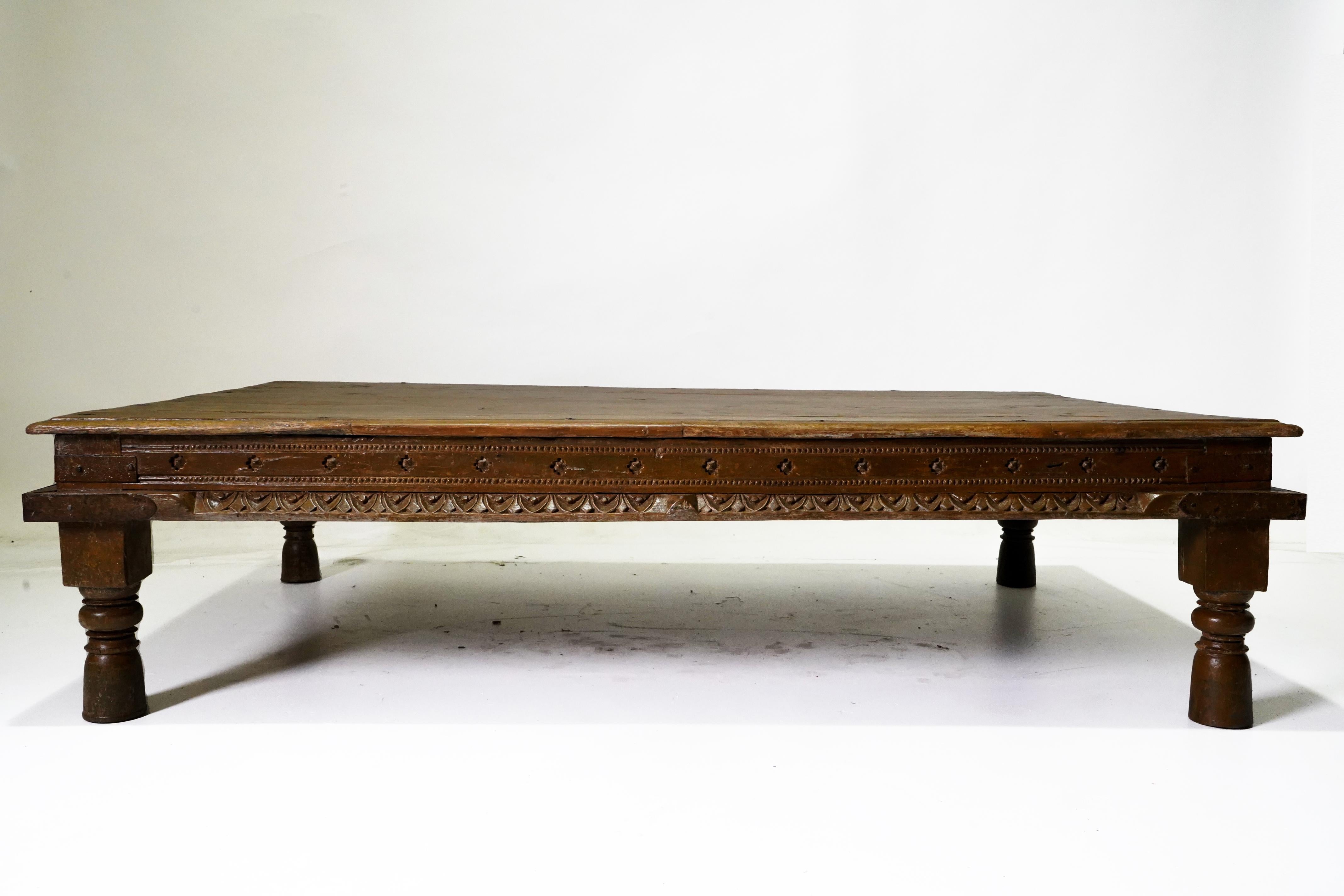 An exceptionally original antique 19th century Indian daybed from Gujarat. The bed, which can be used as a large coffee table, features tall baluster legs and a carved waisted frame supporting a planked top. Metal corner banding and studs provide