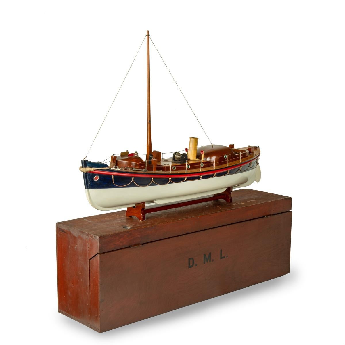A working model of a motor lifeboat by Bassett-Lowke. Boxwood decks, a folding mast, a yellow funnel and a nickel-plated steering wheel. The centre has a removable mid-section which opens to reveal the original electric motor. The lifeboat is set on