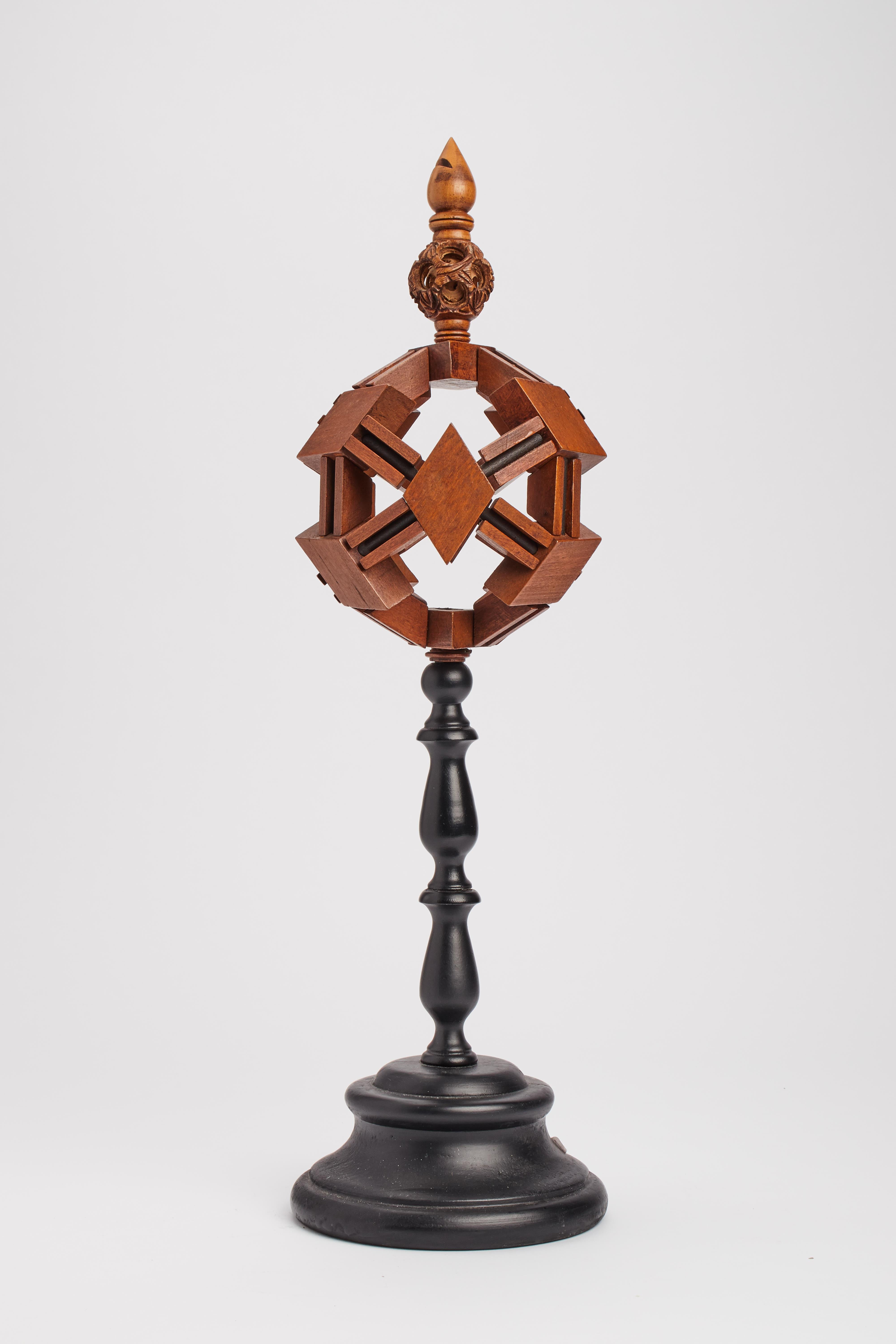 Motivo geometrico in legno massiccio di Oak. La base, in legno di frutta, di forma rotonda, dipinta di nero (ebanizzata), sopra, una sfera costruita da elementi geometrici, tenuti insieme da una corda nera. Sopra c'è una sfera più piccola e tornita,