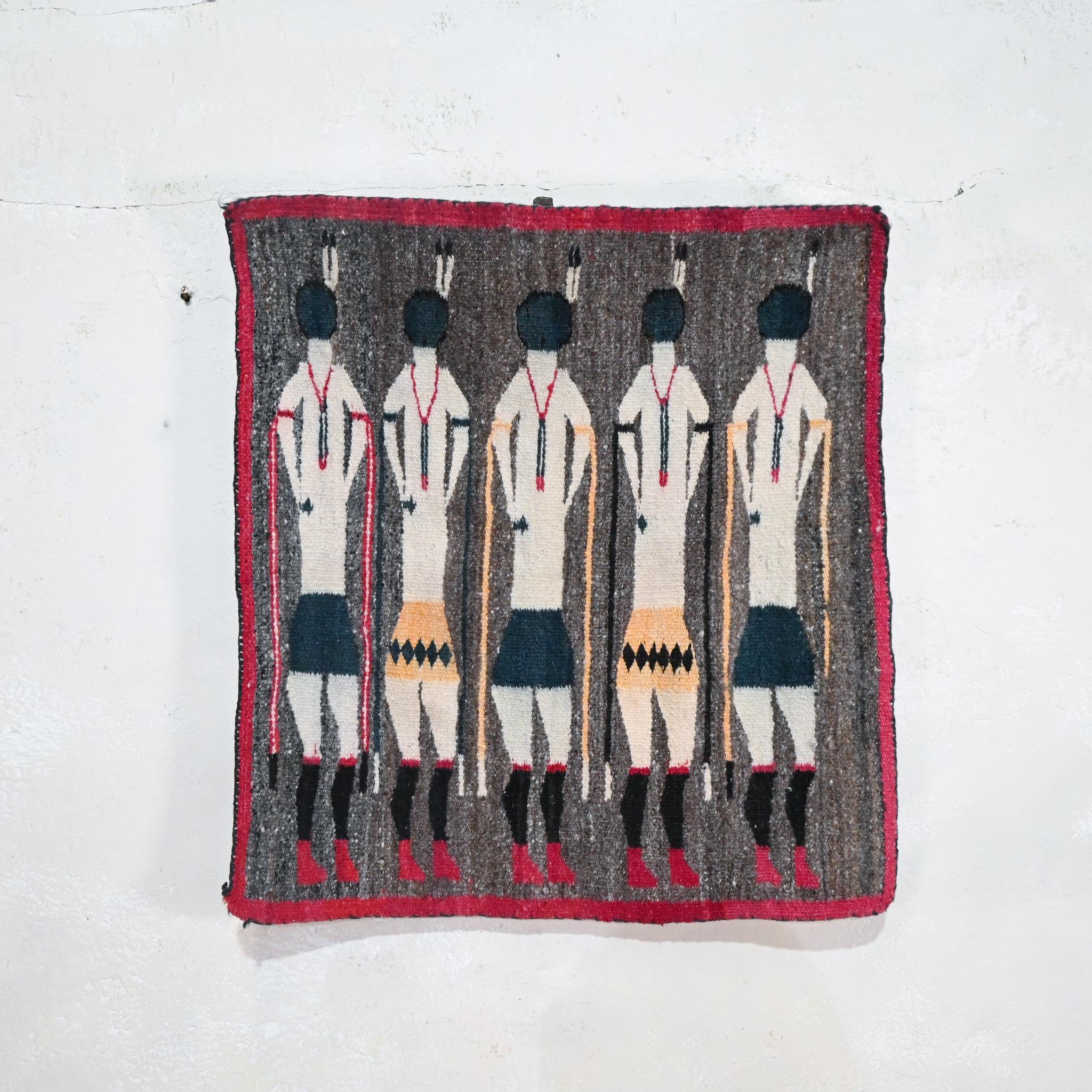 Un colgante de pared Yei Navajo Figural tejido plano de doble cara - hacia 1930. Muestra cinco figuras de pie sobre un fondo gris moteado, enmarcadas por un borde rojo. 
 
La iconografía yei está relacionada con las pinturas de arena religiosas