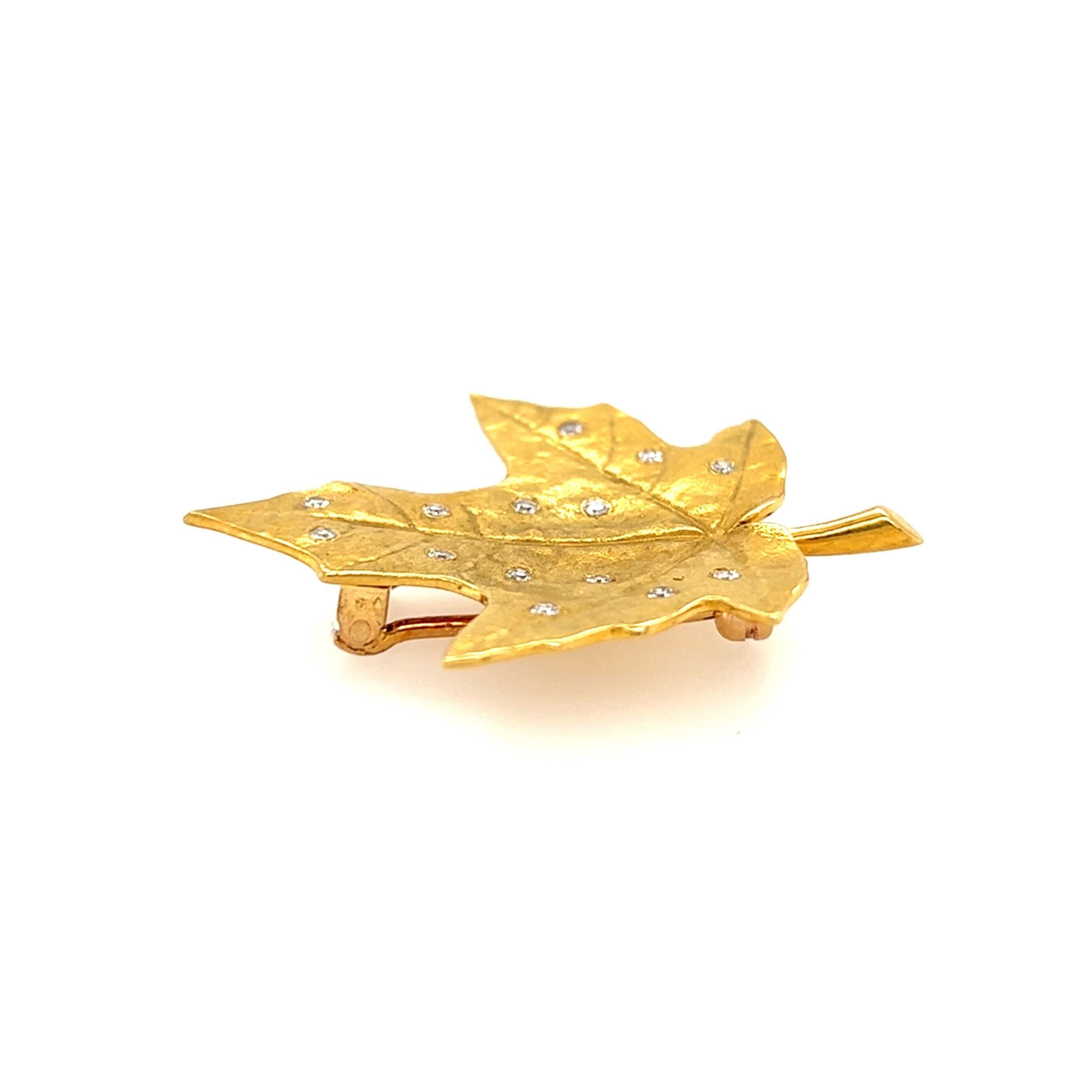 An 18 karat yellow gold and diamond brooch.  Designed as a matte gold maple leaf with incised veining scattered with fourteen (14) brilliant cut diamonds.  Total diamond weight approximately 0.21 carats.  With a 14 karat yellow gold back.  Length