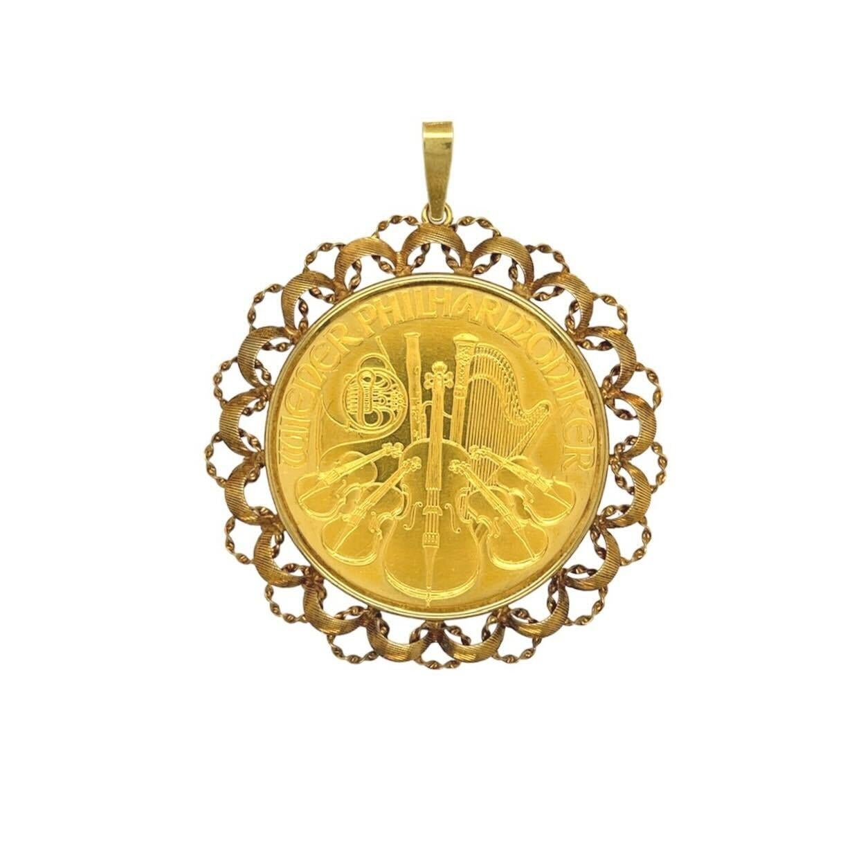 A 24 and 14 karat yellow gold pendant.  The pendant is formed of the 24 karat gold Austrian Vienna Philharmonic coin within a 14 karat gold scrolling ribbon motif frame.  The obverse of the coin depicts the pipe organ of the Vienna Philharmonic